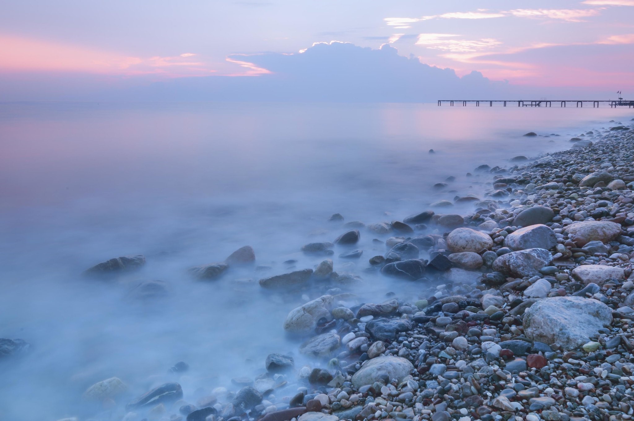 Pebble beach with calm ocean and pier at sunset HD Wallpaper