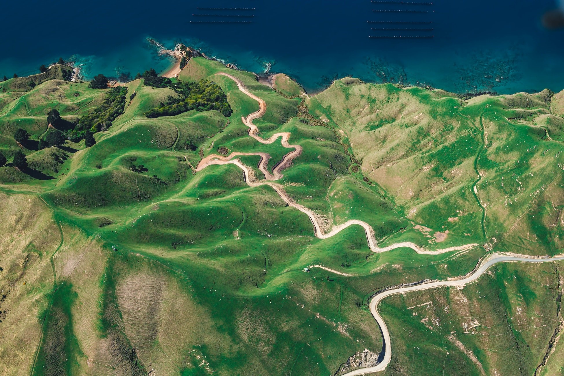 Aerial view of winding road through green hills by the sea HD Wallpaper
