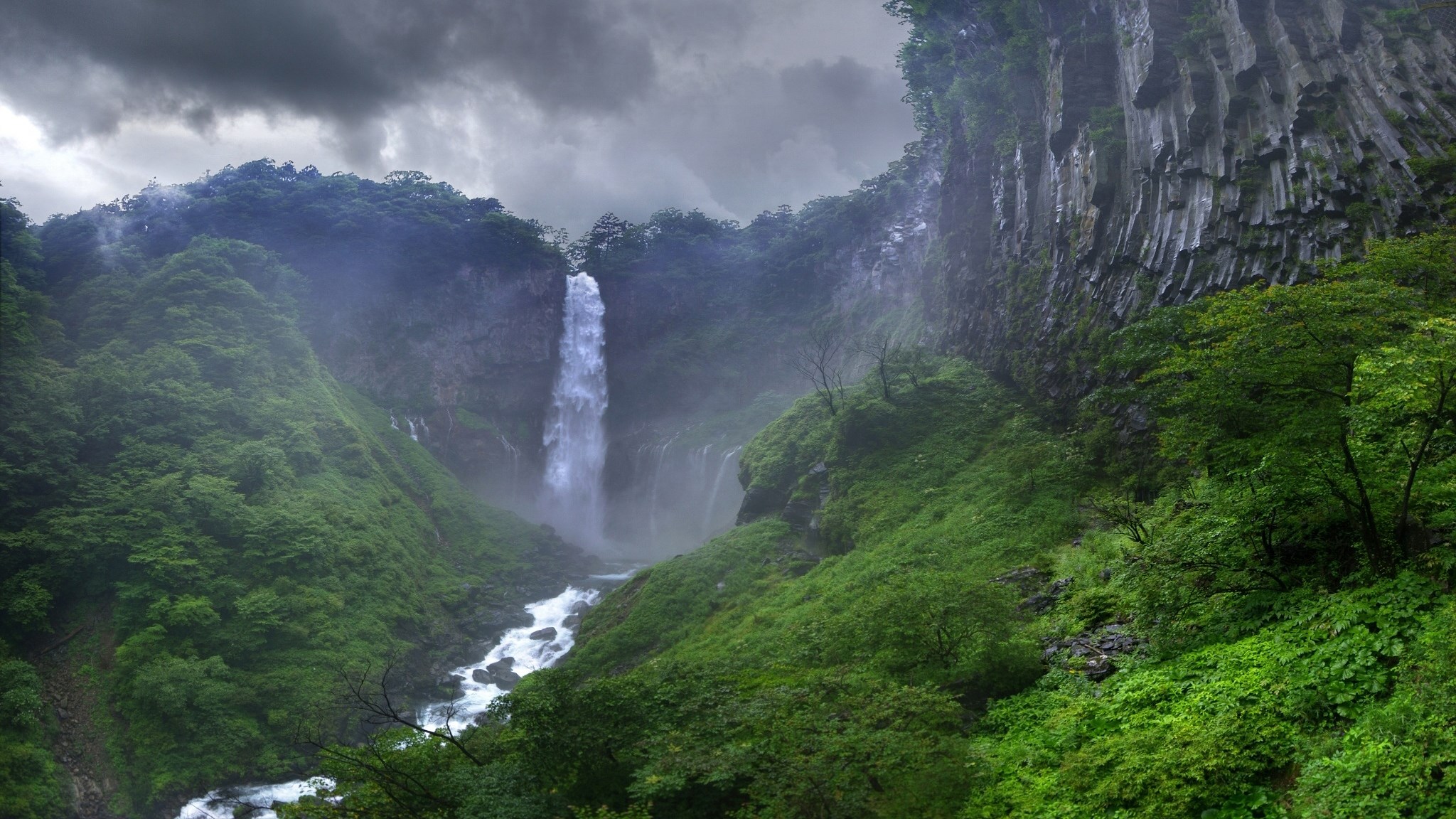 Waterfall cascading down a rocky cliff into a river HD Wallpaper