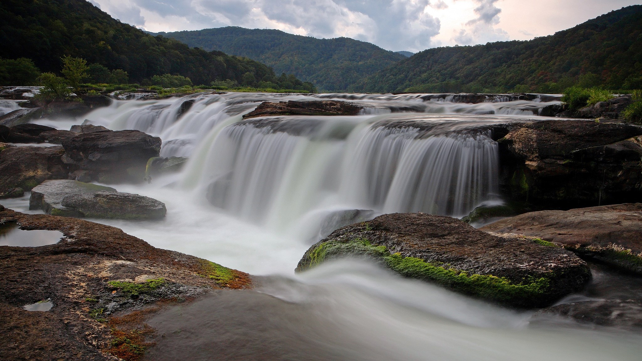 Waterfall cascading over rocks in a mountain valley HD Wallpaper