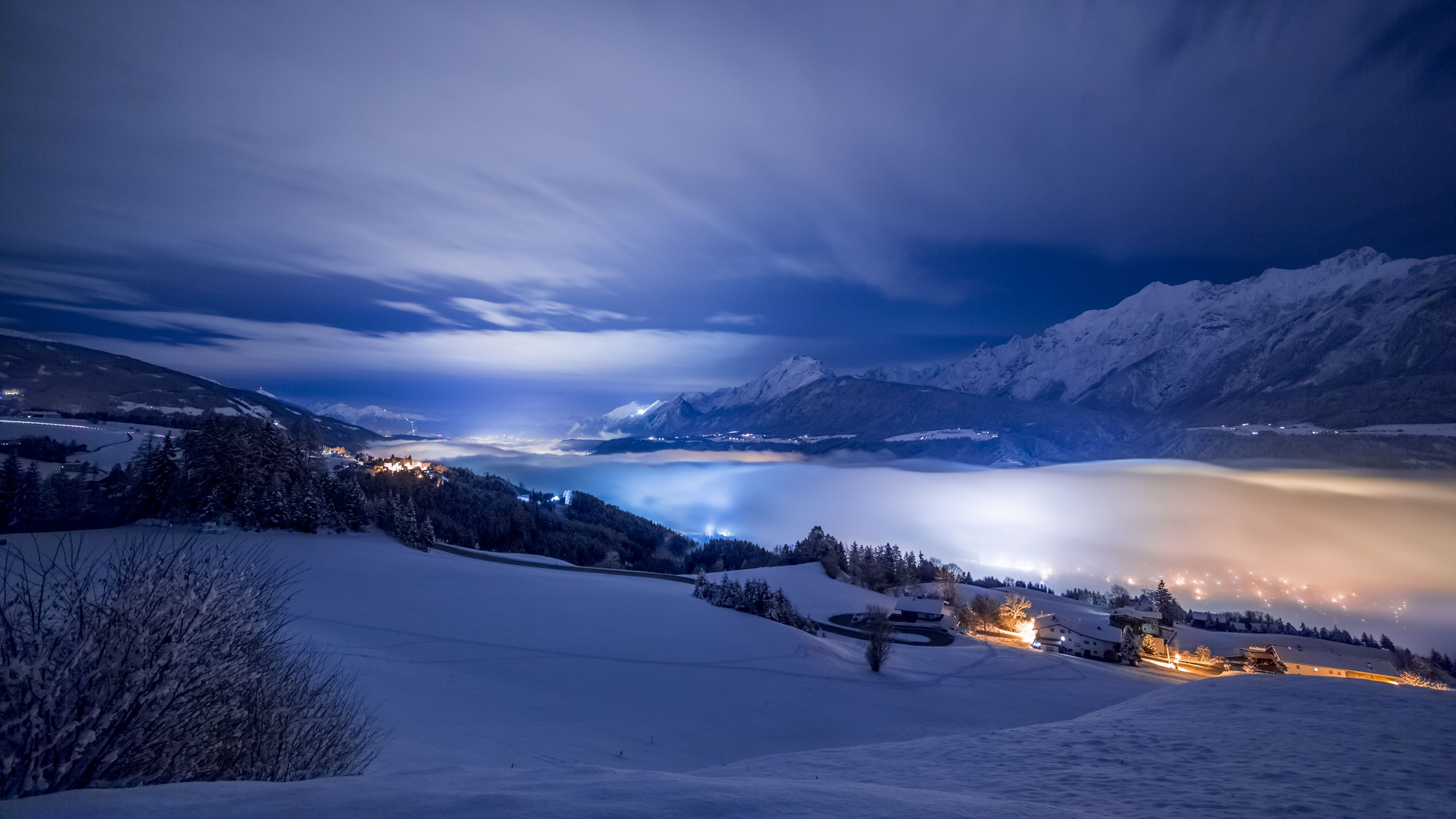 Snowy mountains at night with fog and village lights HD Wallpaper