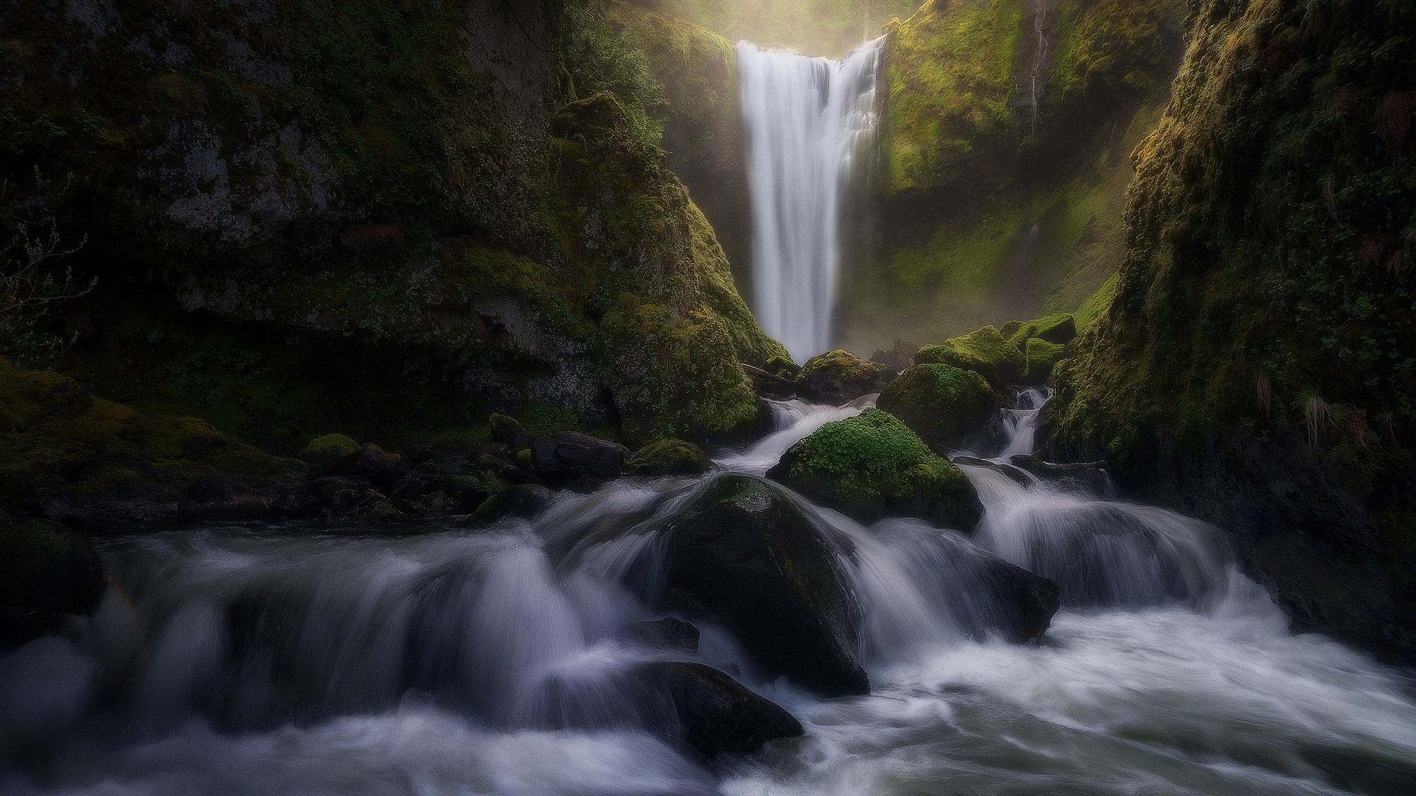 Waterfall cascading over moss-covered rocks in a misty forest HD Wallpaper