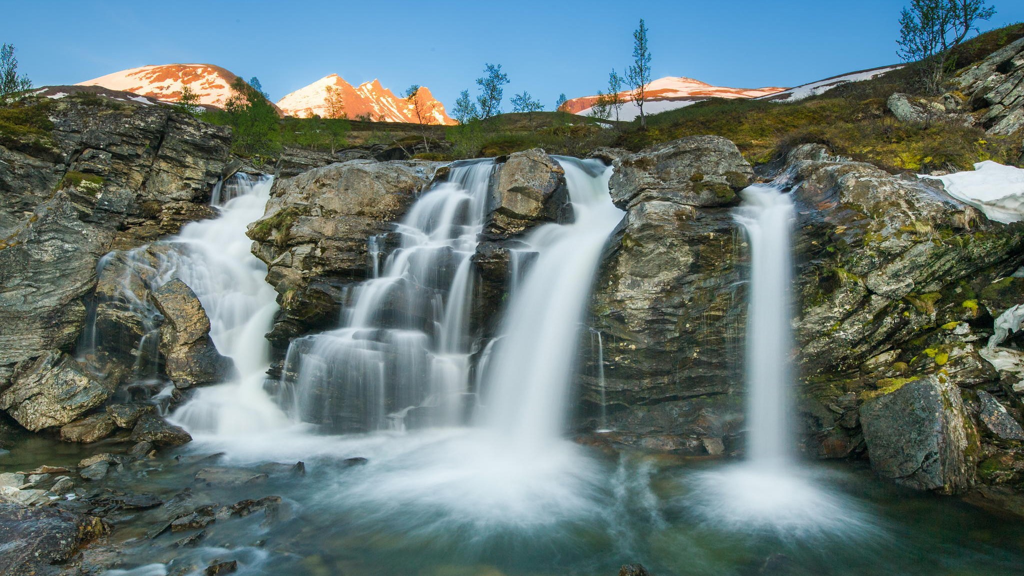 Waterfall cascading over rocks with mountains in background HD Wallpaper