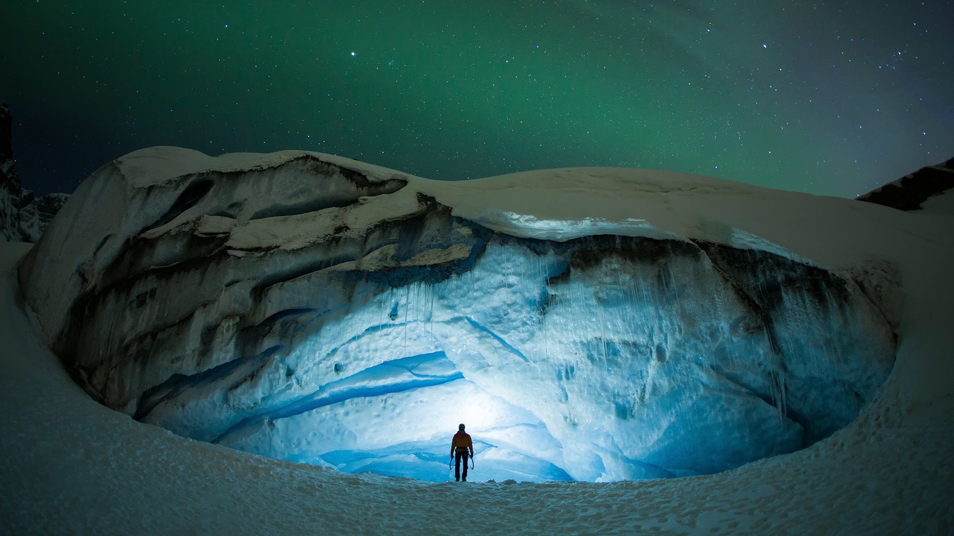 Person in illuminated ice cave under aurora borealis HD Wallpaper