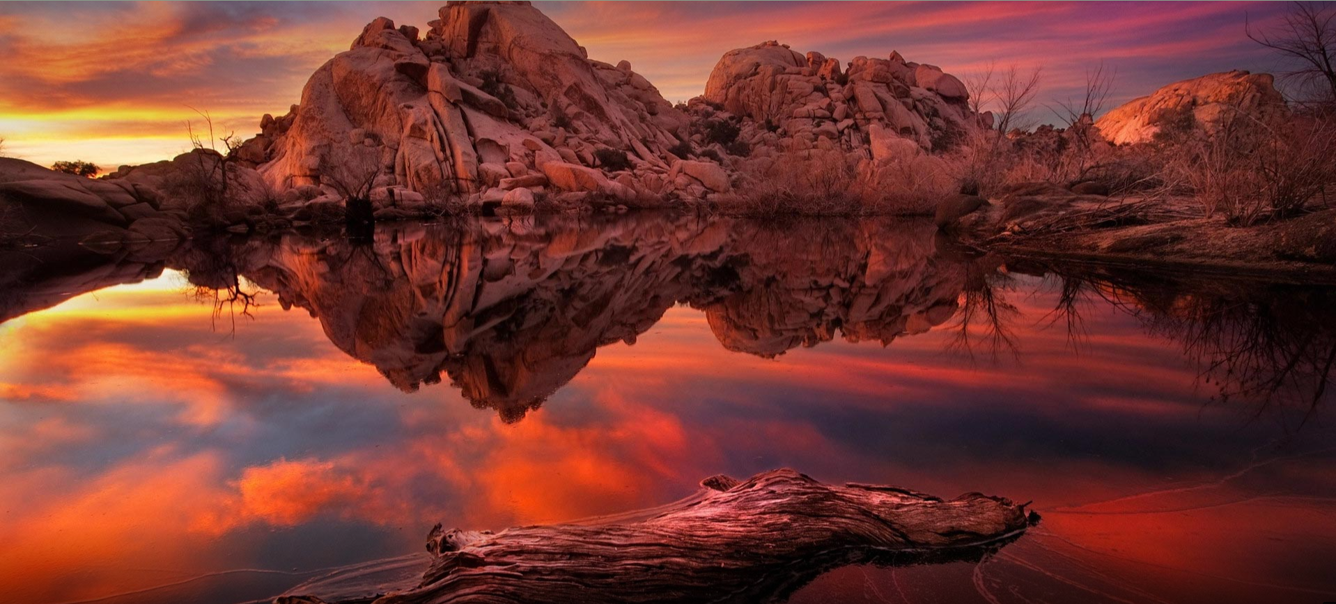 Sunset reflection on water with rocks and driftwood HD Wallpaper