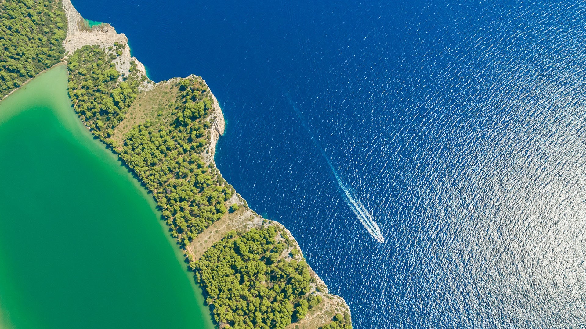 Aerial view of a boat sailing on the blue sea near a green coast HD Wallpaper