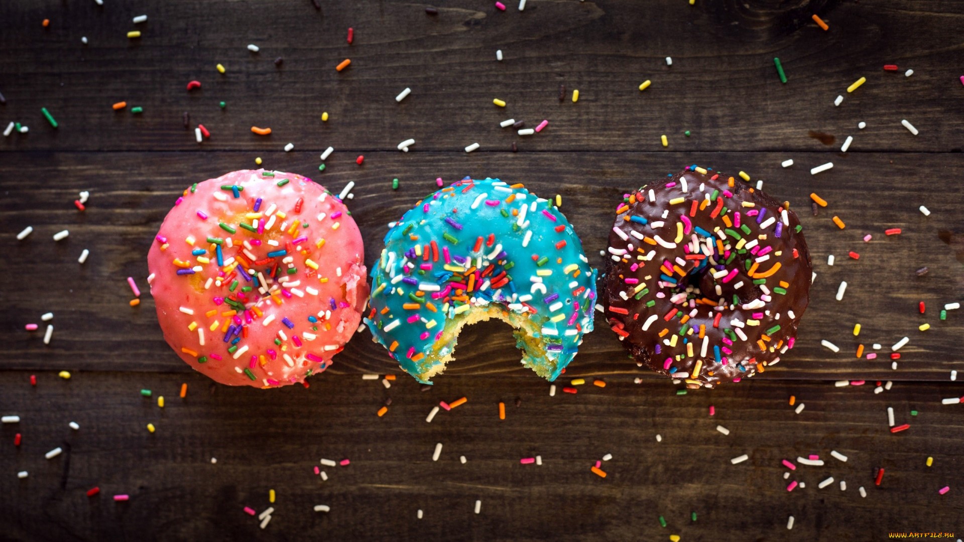 Three colorful donuts with sprinkles on a wooden table HD Wallpaper