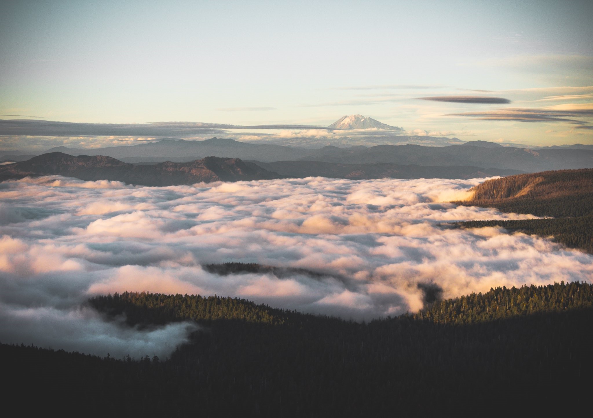 Mountain range above clouds with distant snow-capped peak HD Wallpaper