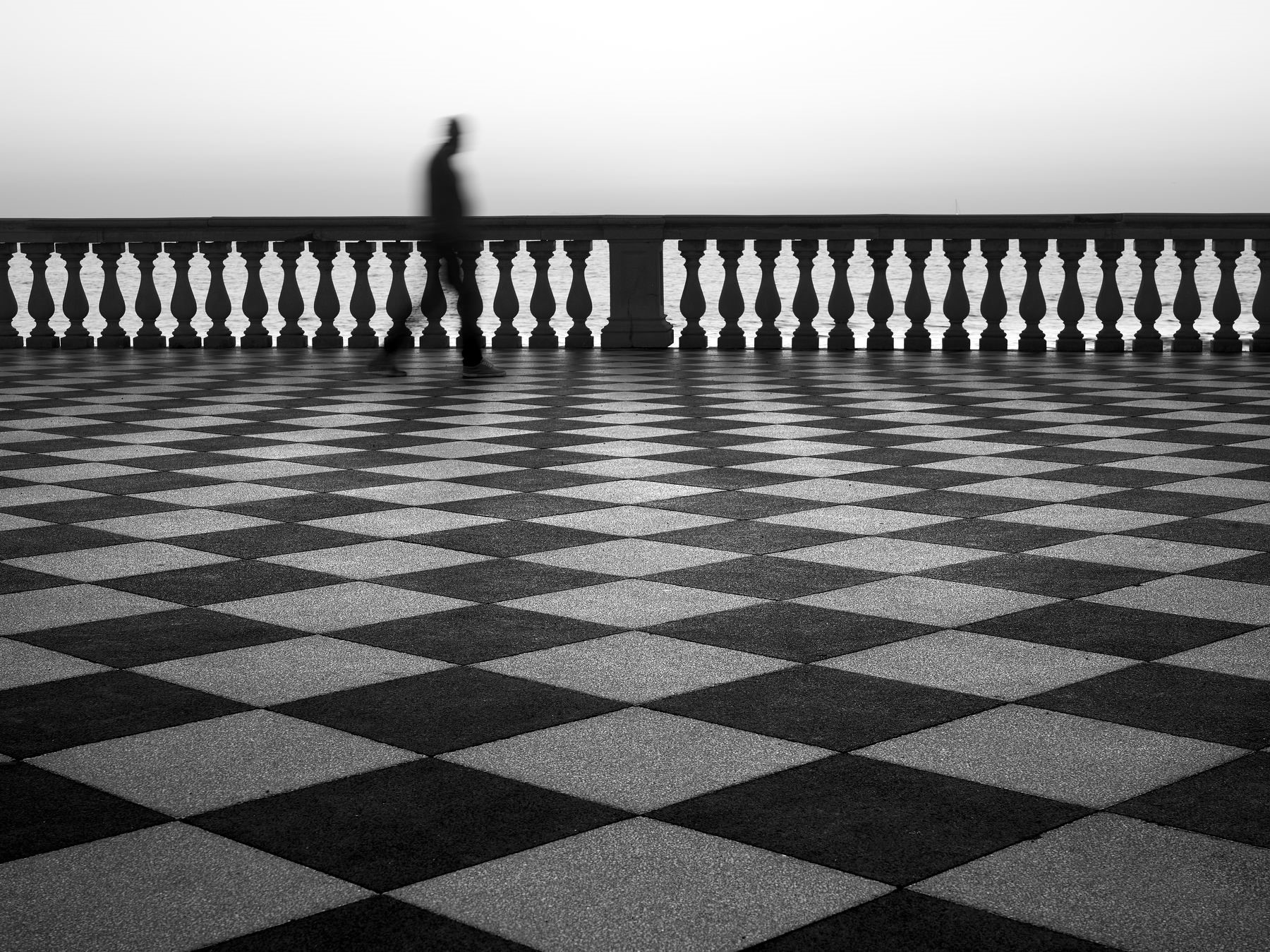 Man walking on checkered pavement by the sea HD Wallpaper
