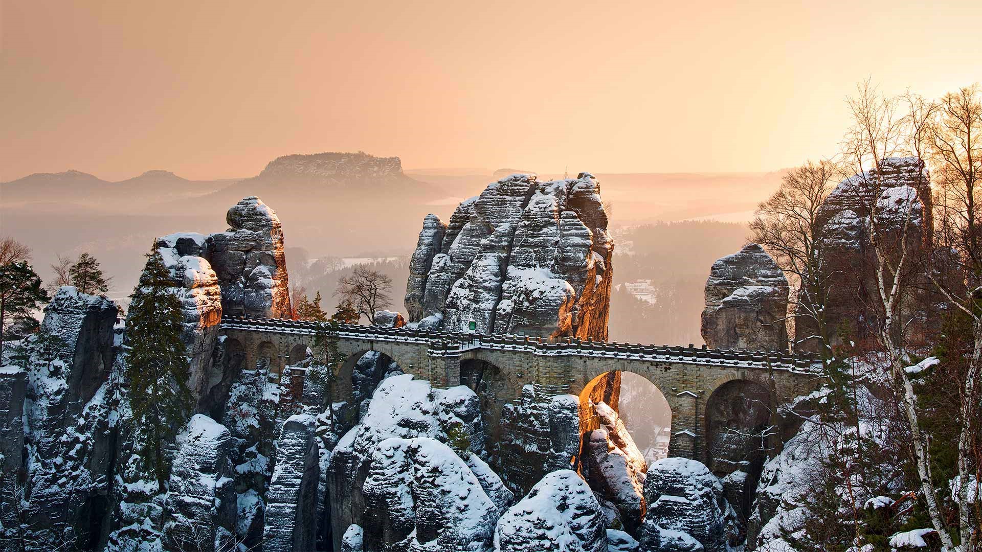 Snow-covered rock formations with a bridge at sunrise HD Wallpaper