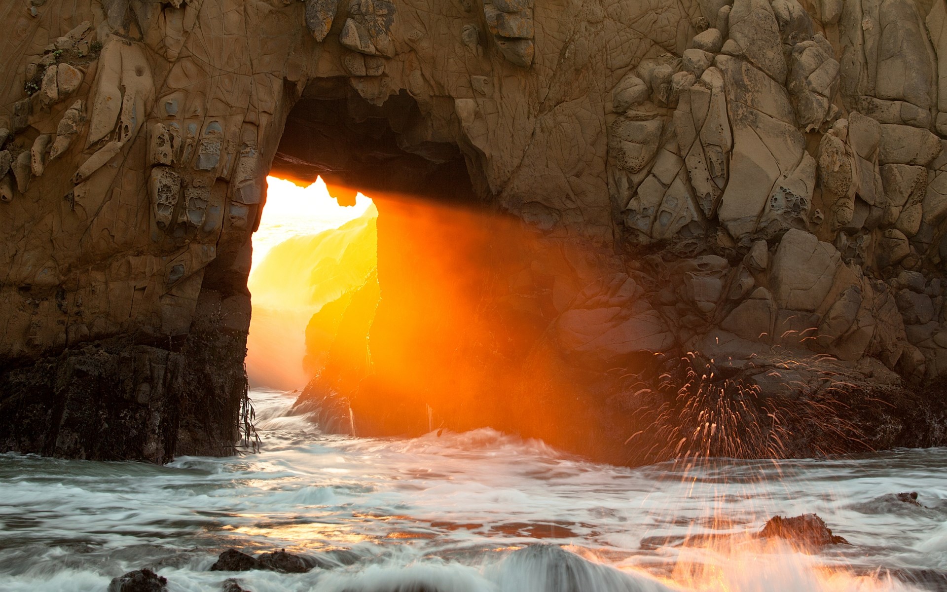 Sunlight beams through a sea cave archway onto ocean waves HD Wallpaper