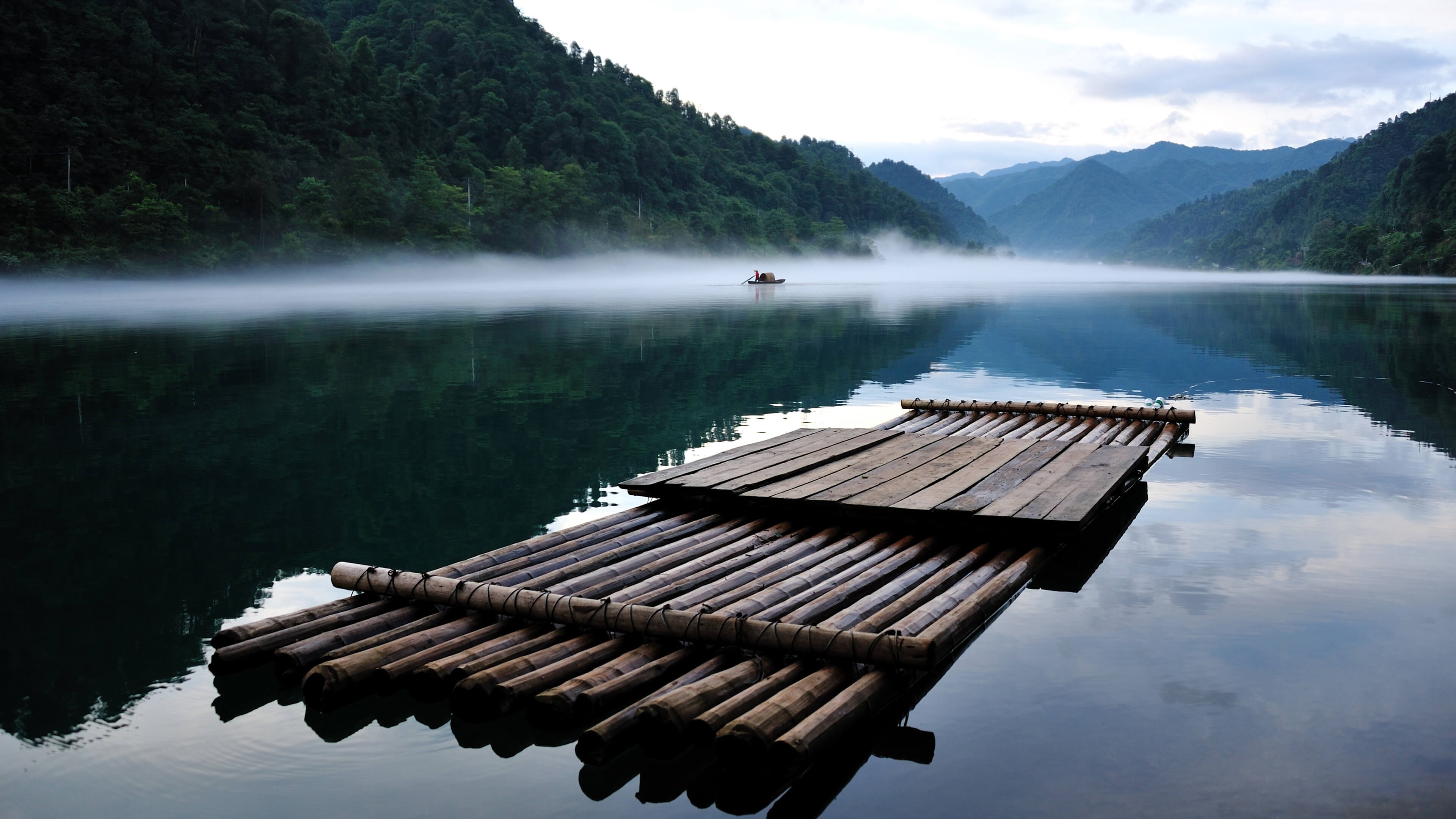 Bamboo raft on a misty lake with mountains HD Wallpaper