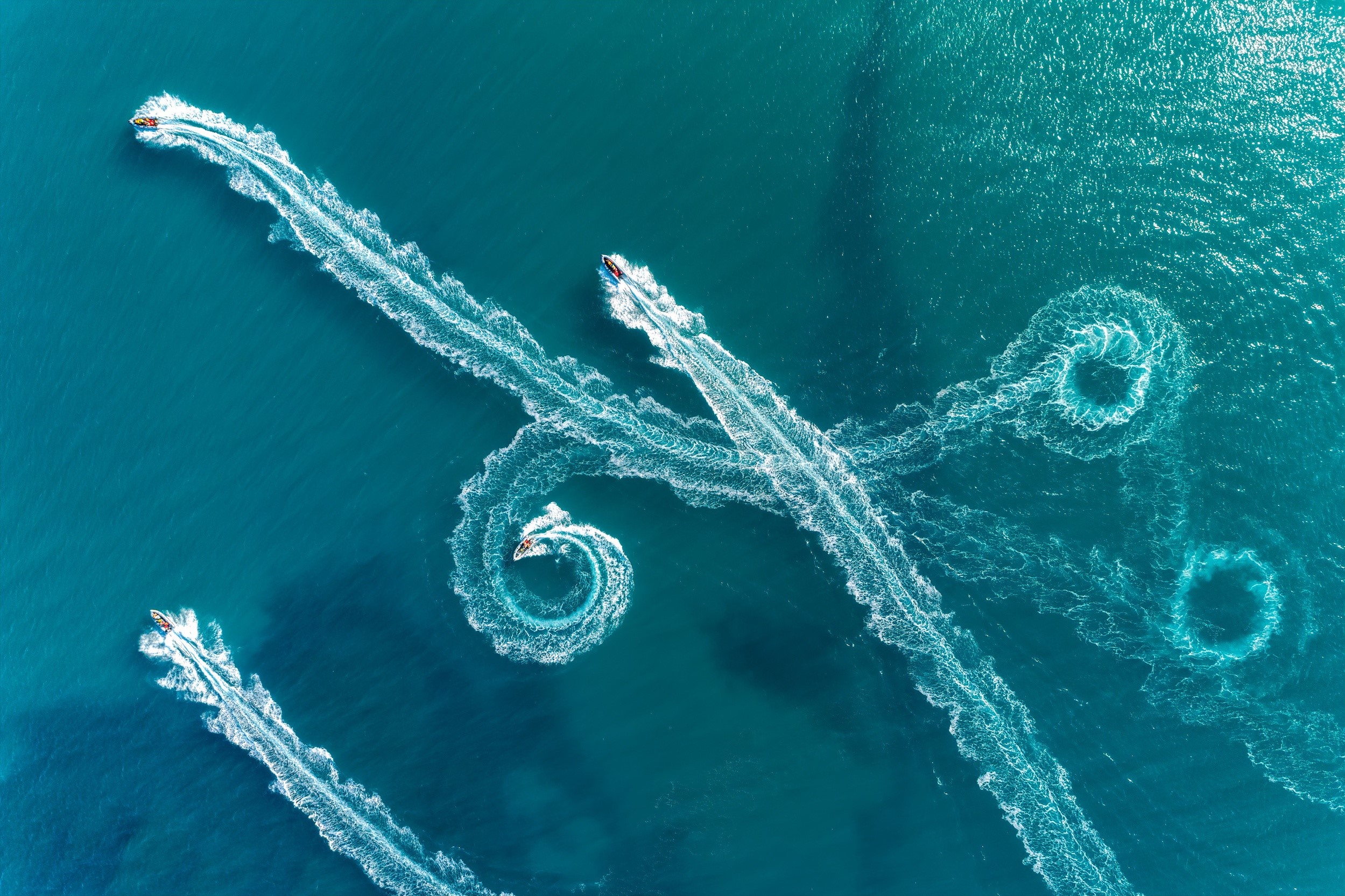 Jet skis creating water trails in the sea HD Wallpaper