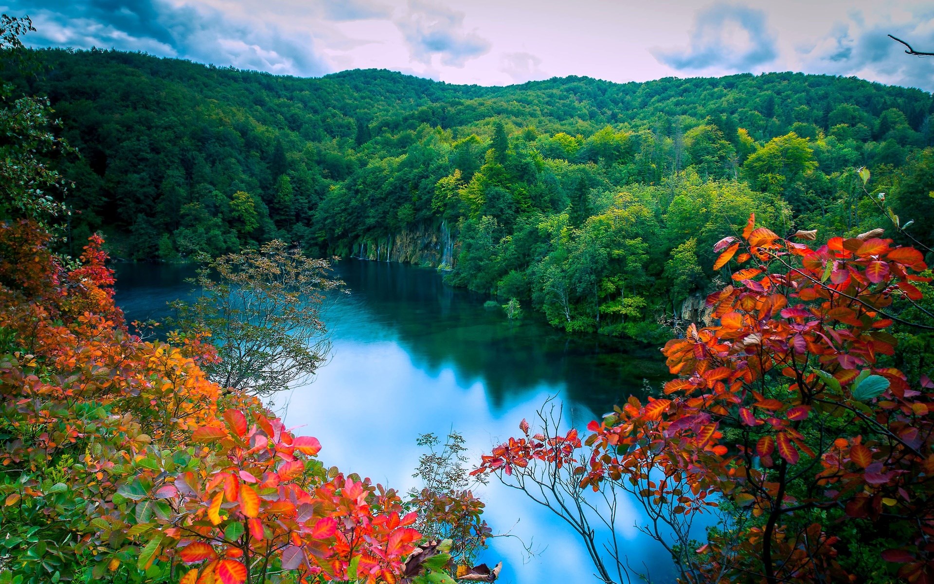 Autumn leaves frame a tranquil lake surrounded by forested hills HD Wallpaper