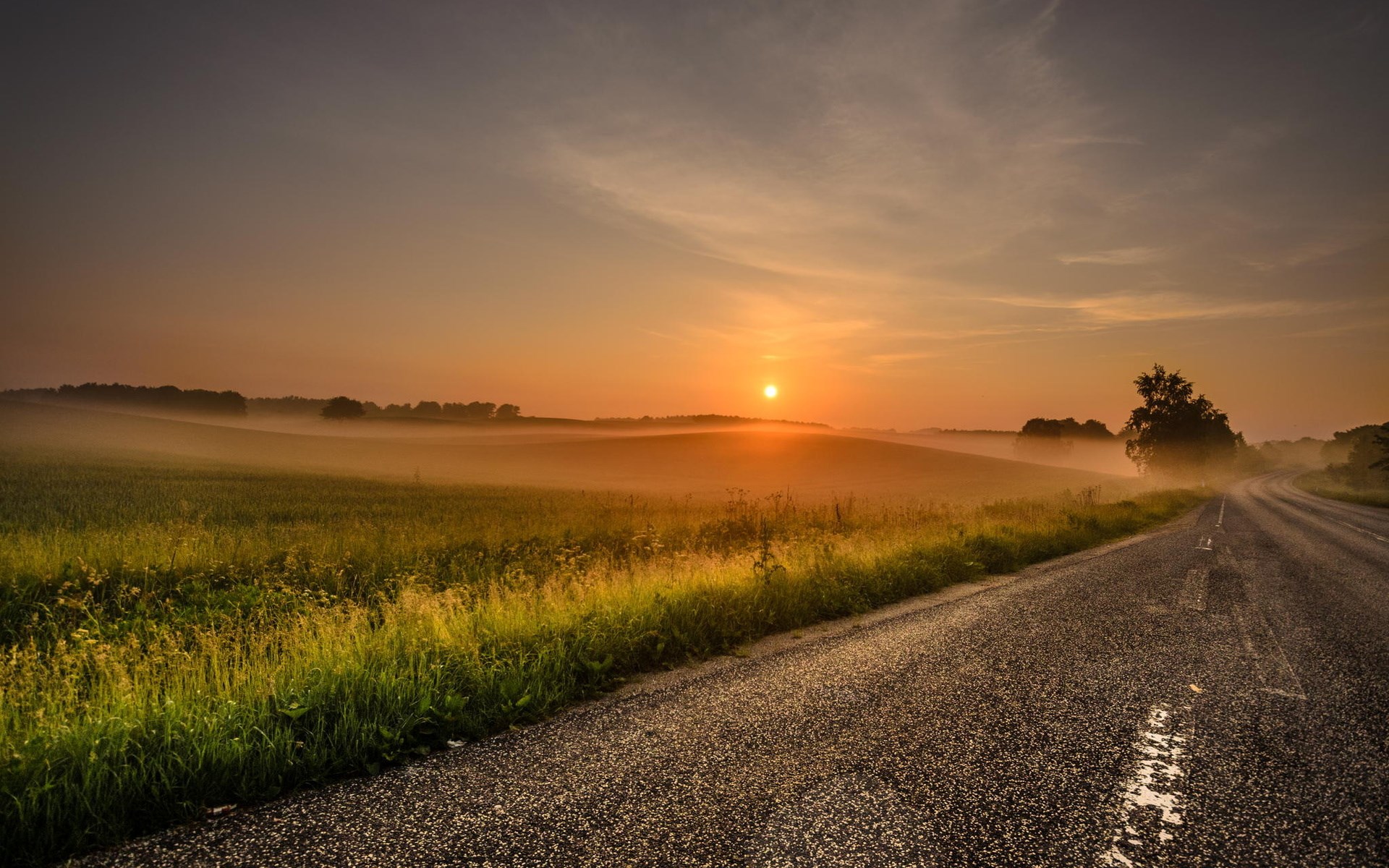 Sunrise over a misty rural landscape with a road HD Wallpaper