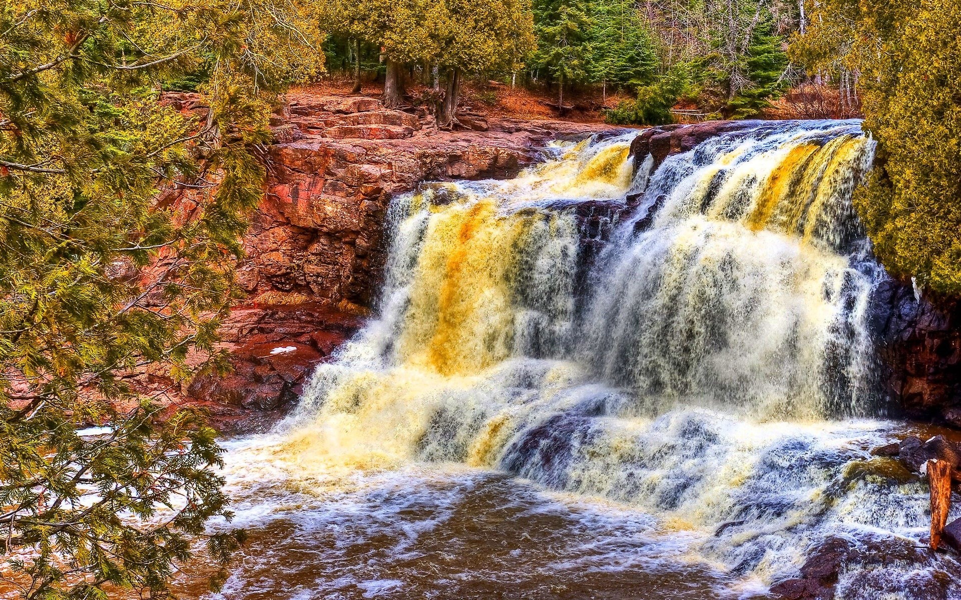 Waterfall cascading over red rocks in autumn forest HD Wallpaper