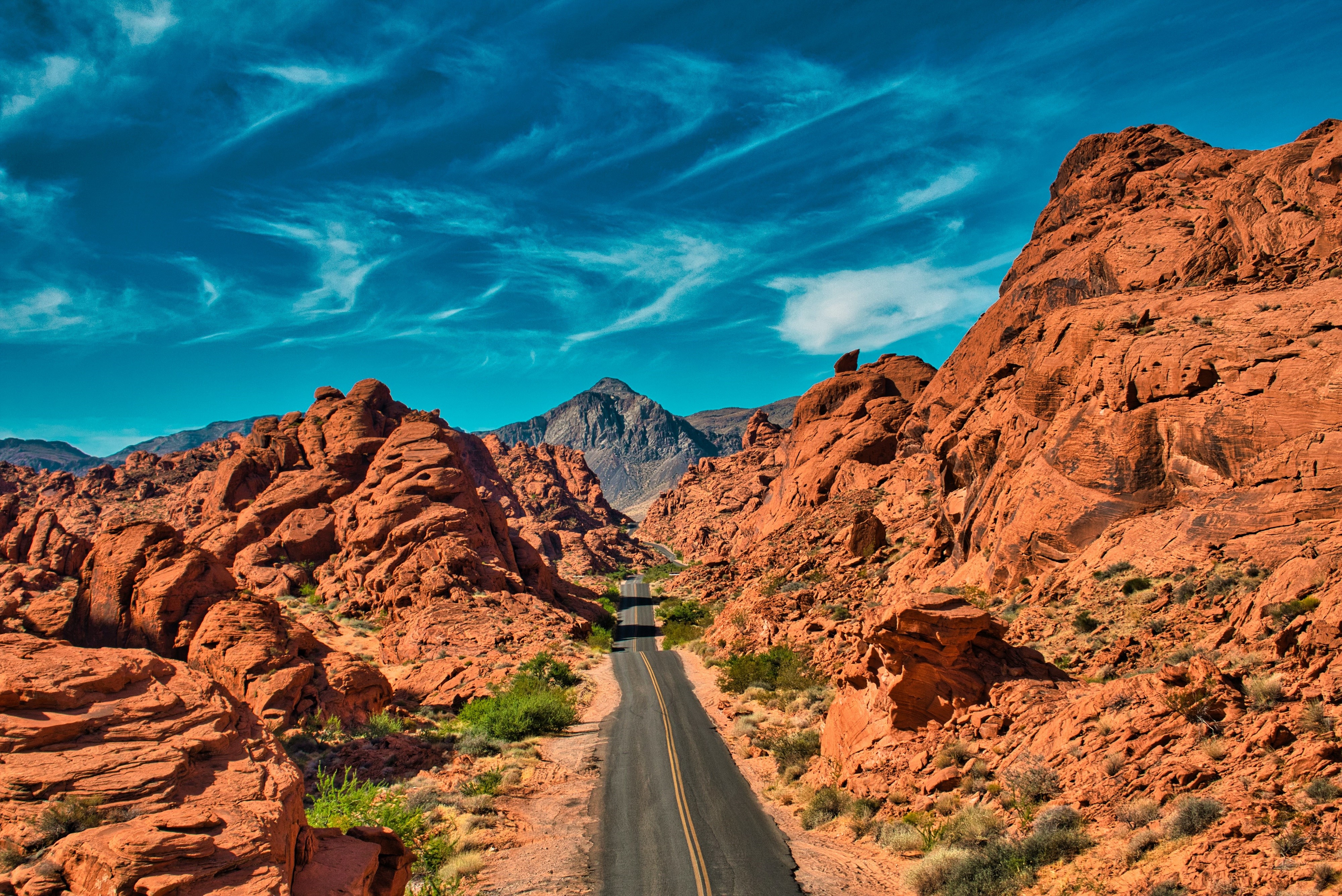Desert road through red rock formations under blue sky HD Wallpaper