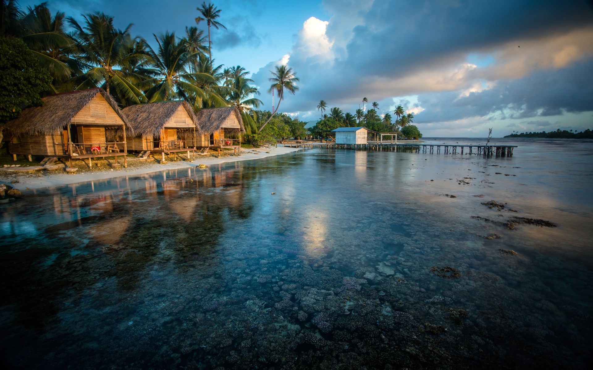 Tropical bungalows on a beach with clear water and pier HD Wallpaper