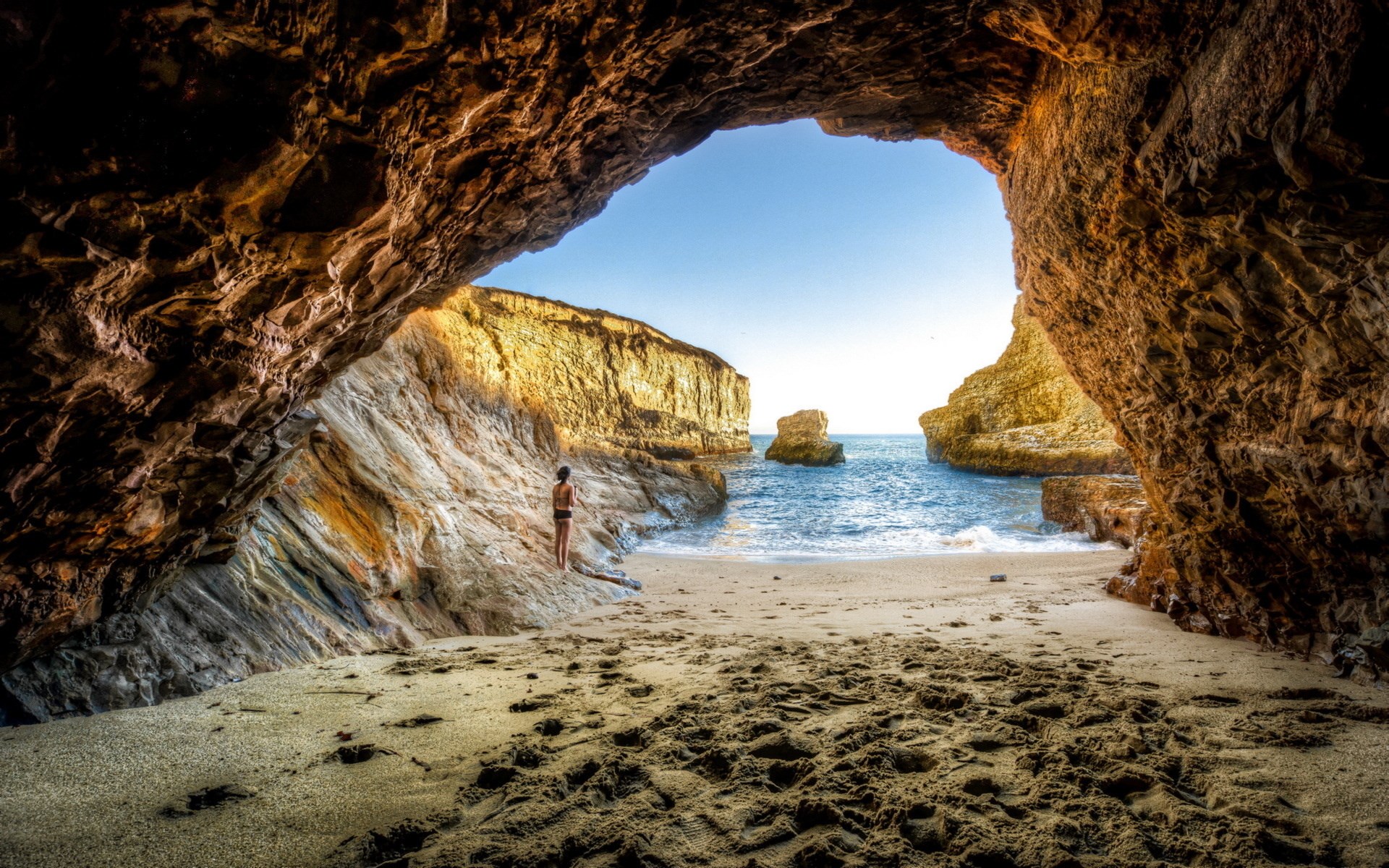 Woman standing on a beach inside a cave HD Wallpaper