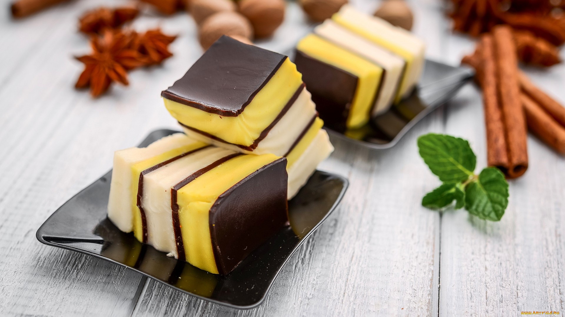 Layered cakes with chocolate, yellow, and white layers on black plates with spices HD Wallpaper