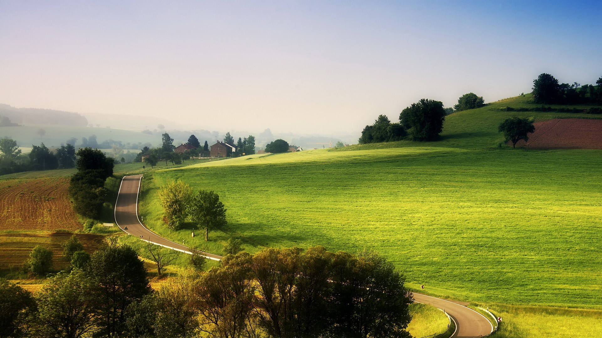 Winding road through rolling green hills and farmland HD Wallpaper