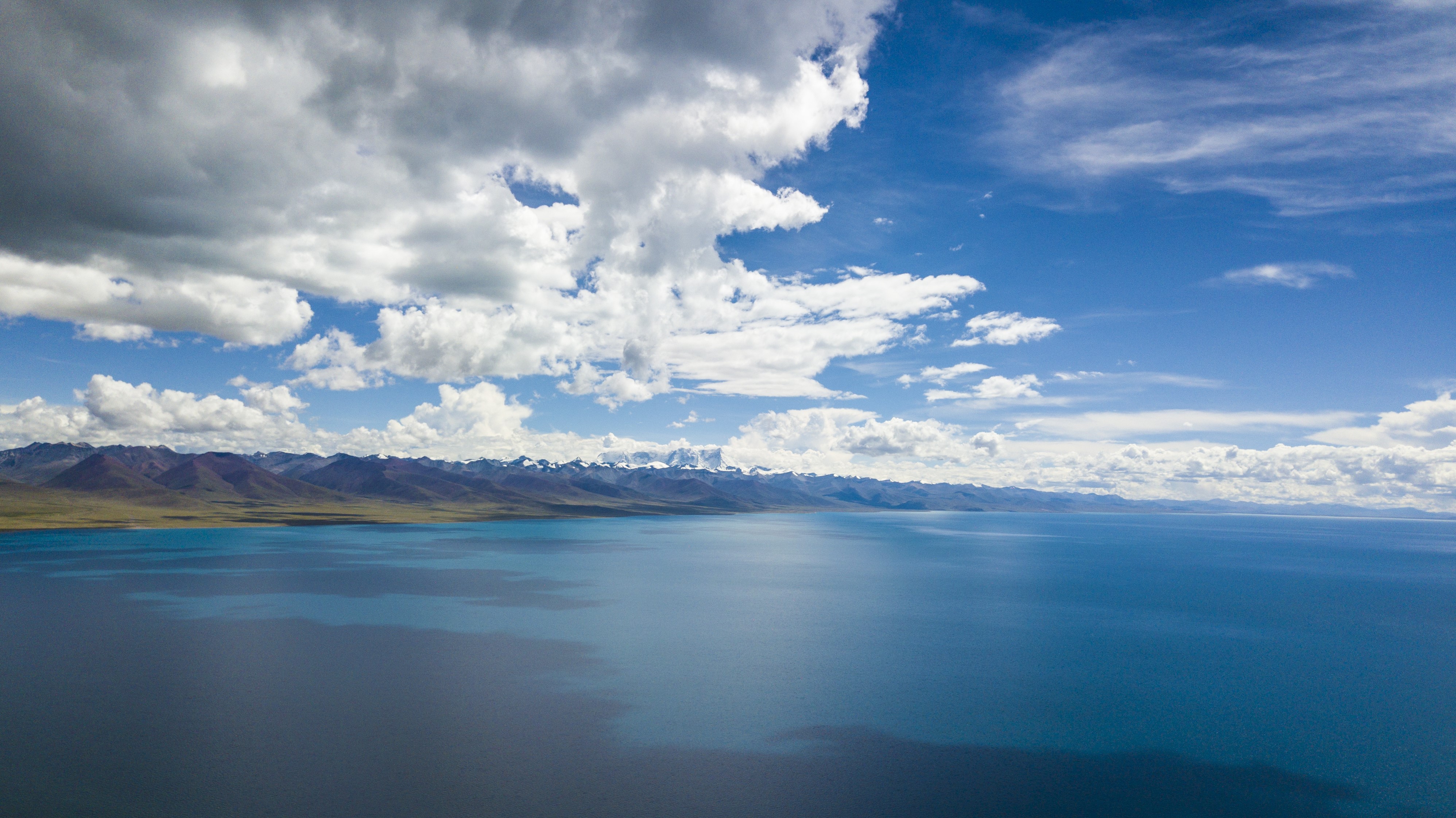 Vast blue lake with snow-capped mountains under clouds HD Wallpaper