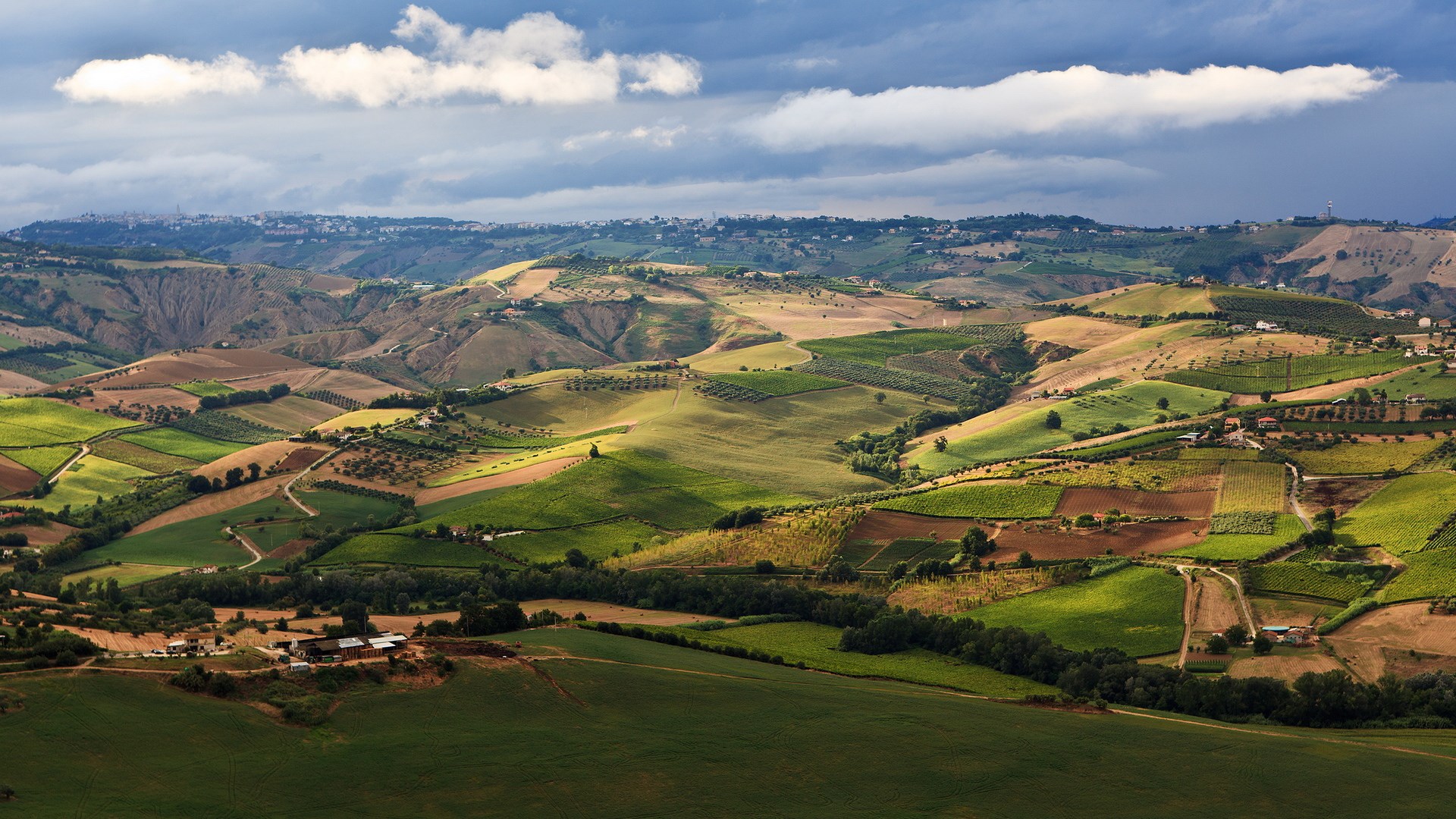 Rolling hills with agricultural fields and a distant town HD Wallpaper