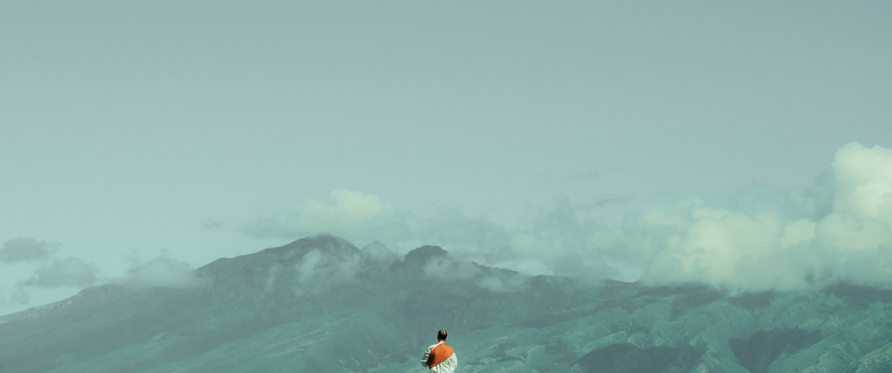 Person in orange and white standing on a mountain overlooking misty mountains HD Wallpaper