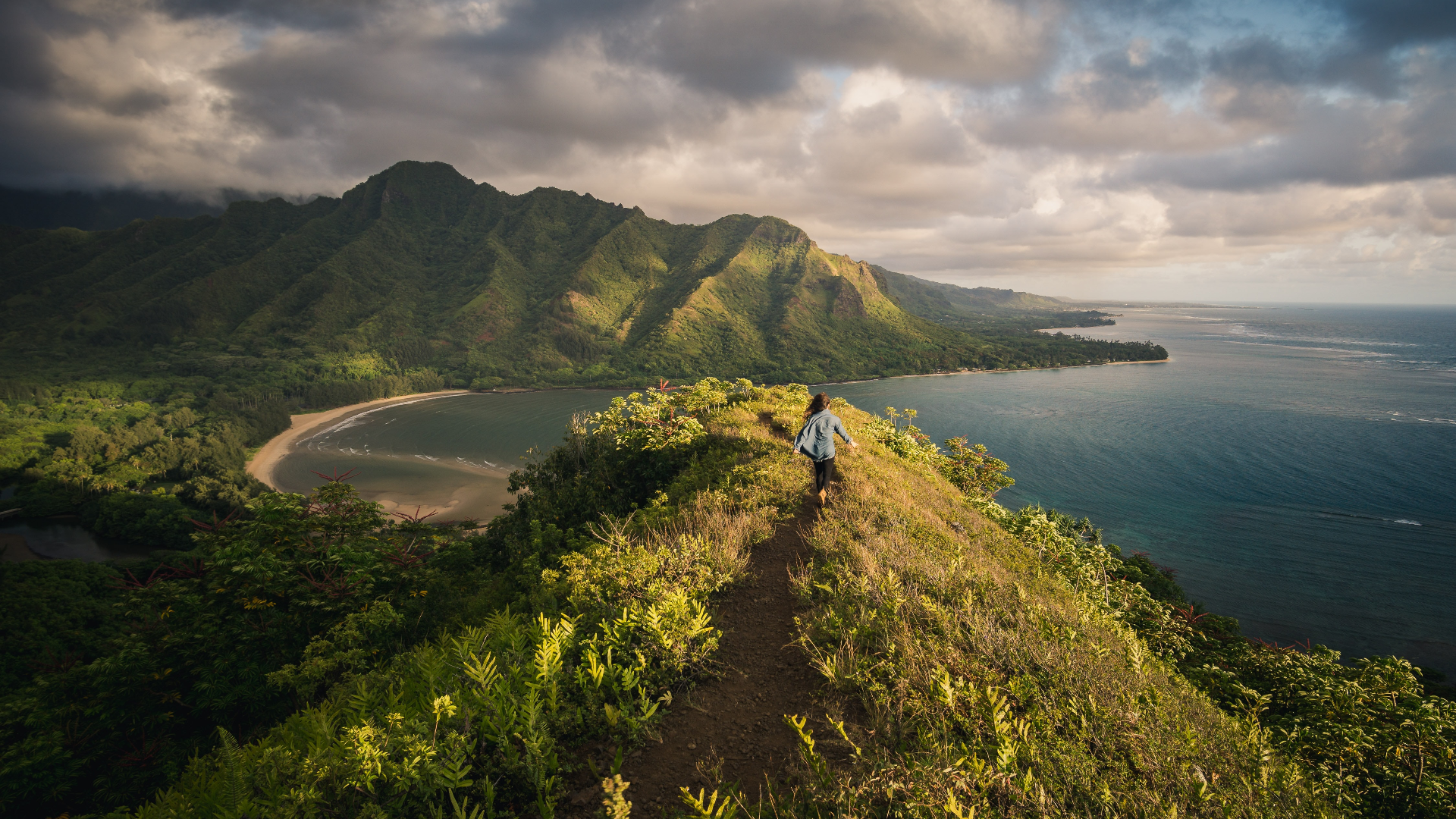 Woman hiking on a ridge overlooking a bay and mountains HD Wallpaper