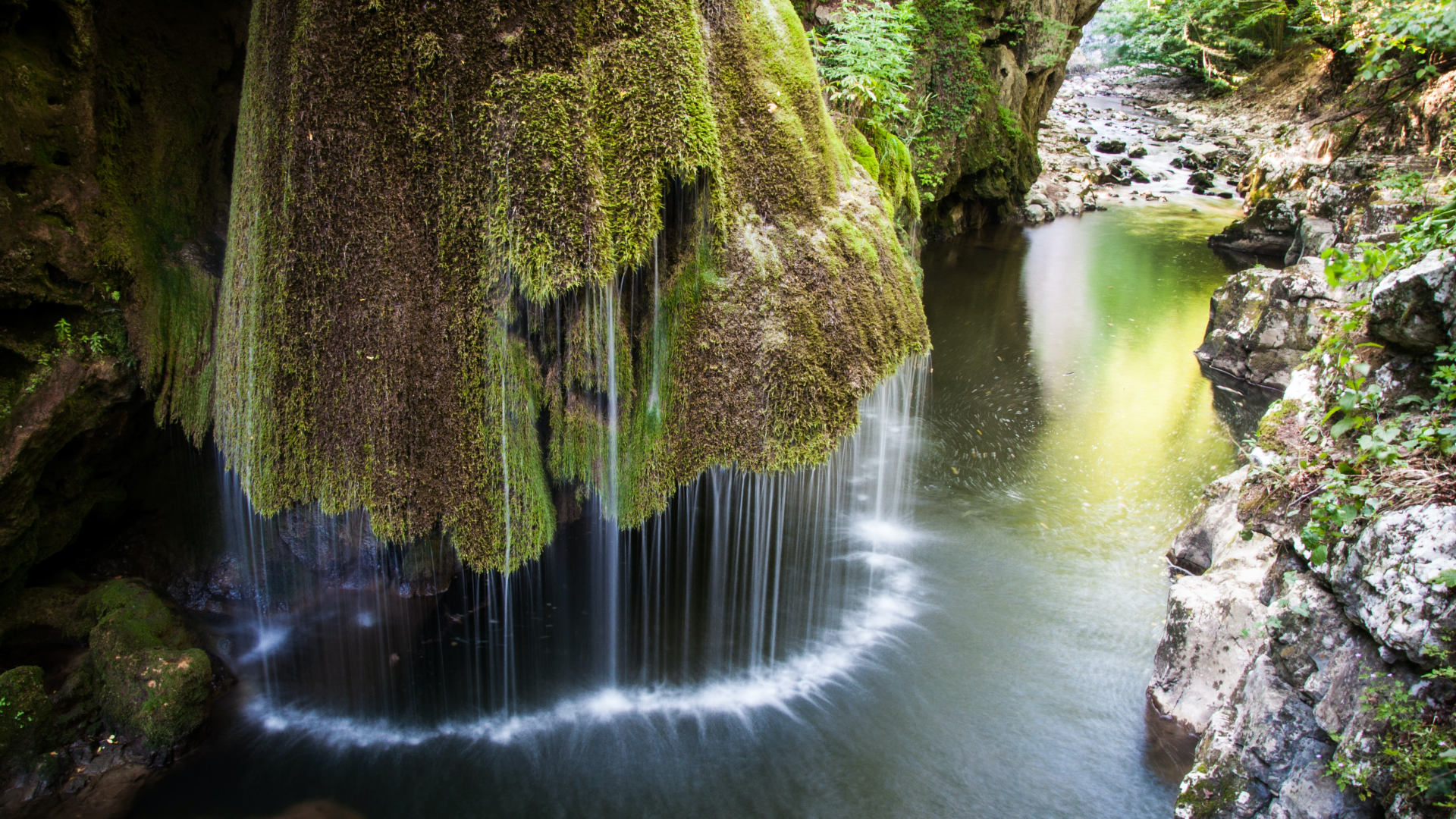 Moss-covered waterfall cascading into a rocky river HD Wallpaper