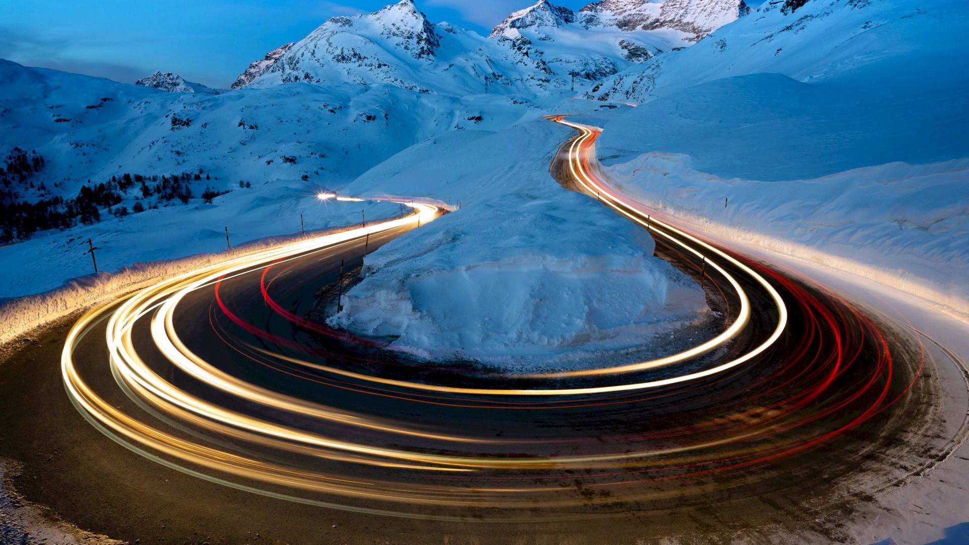 Light trails on a snowy mountain road at dusk HD Wallpaper