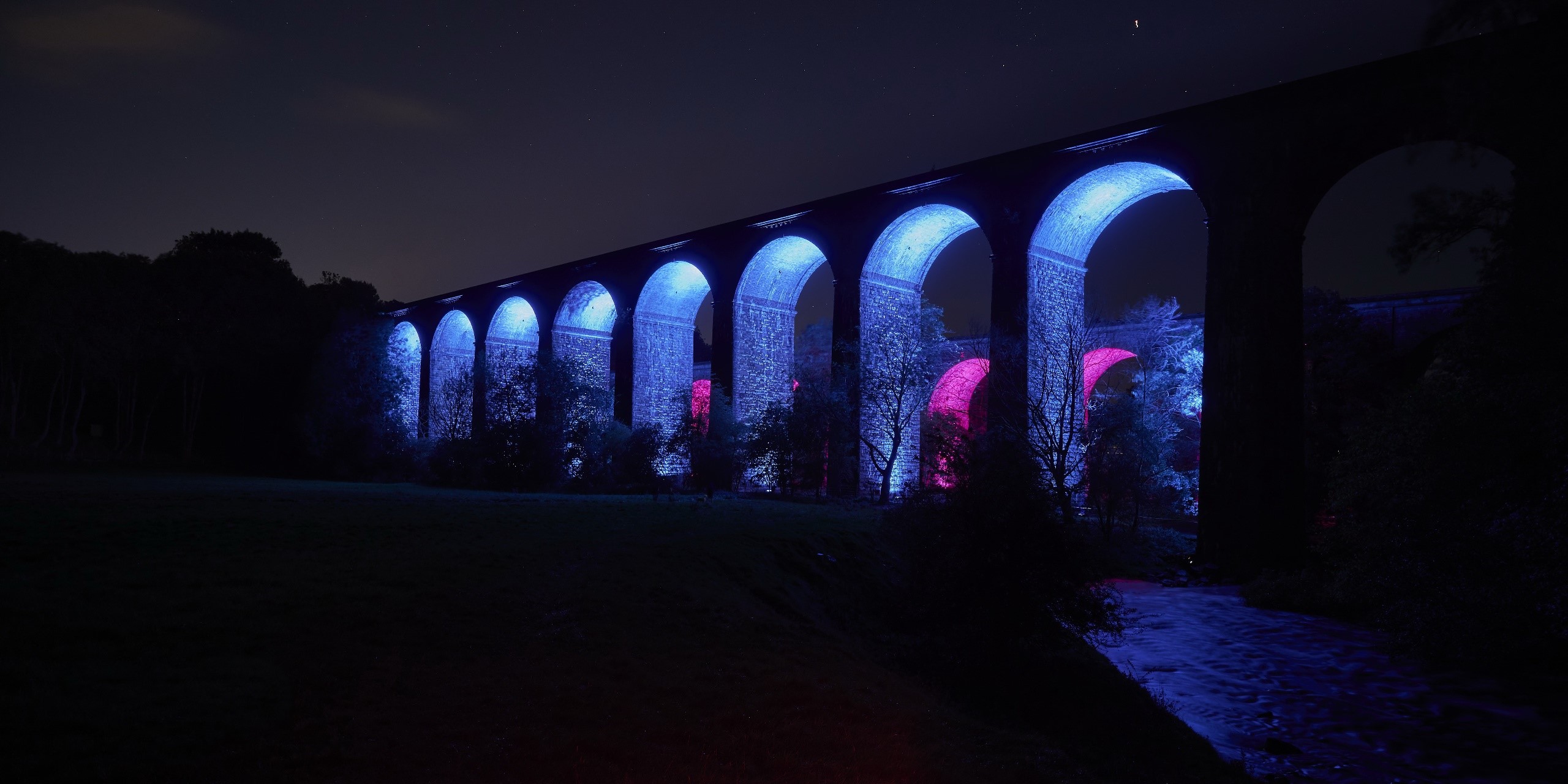 Viaduct illuminated with blue and pink lights at night HD Wallpaper