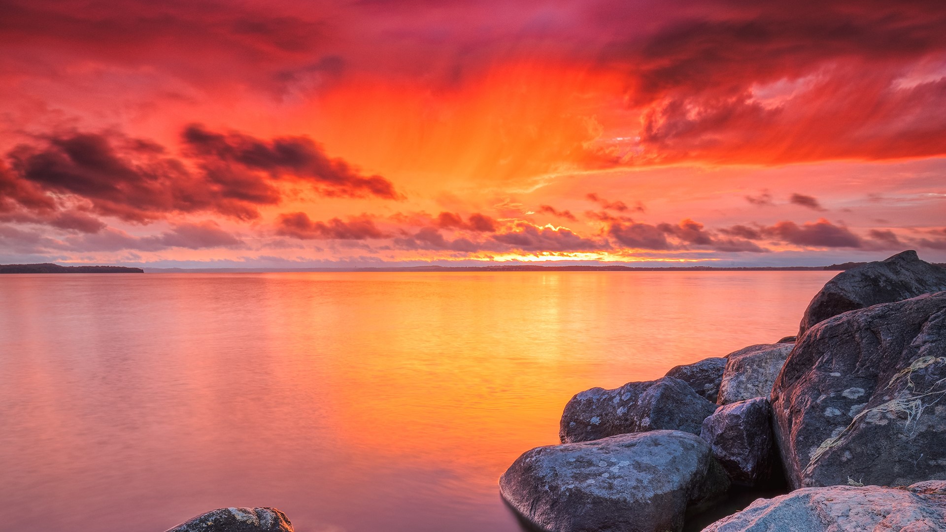 Sunset over a calm lake with rocks in the foreground HD Wallpaper