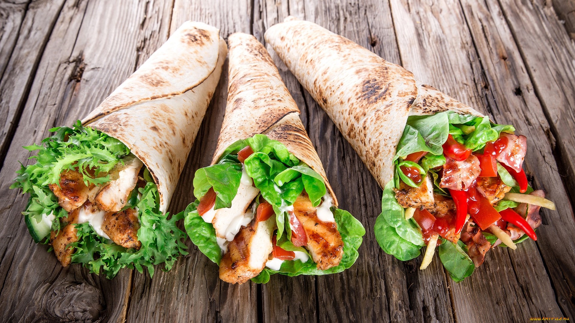 Three chicken wraps with salad and vegetables on a wooden table HD Wallpaper