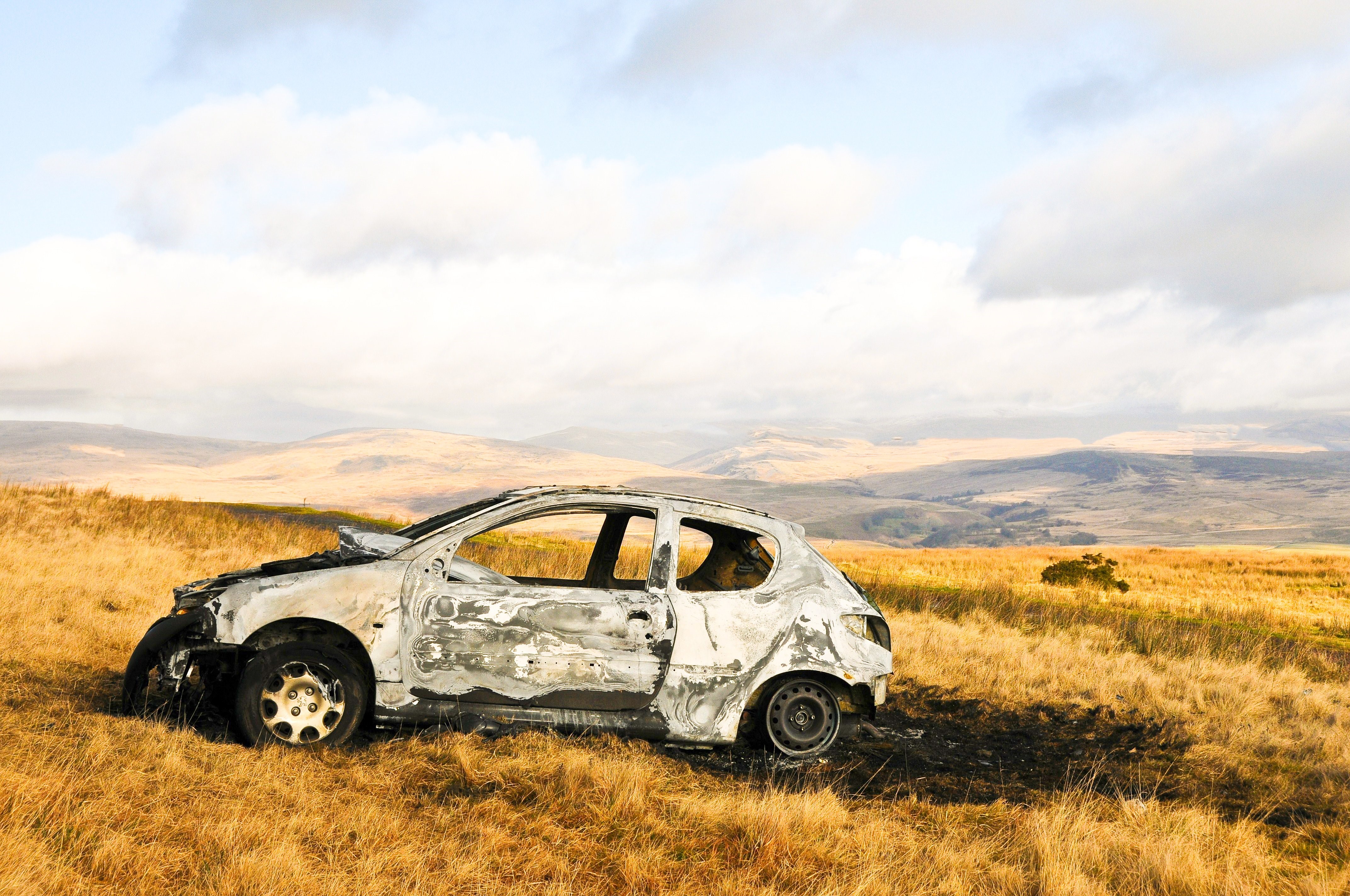Burned Peugeot car in a grassy field HD Wallpaper