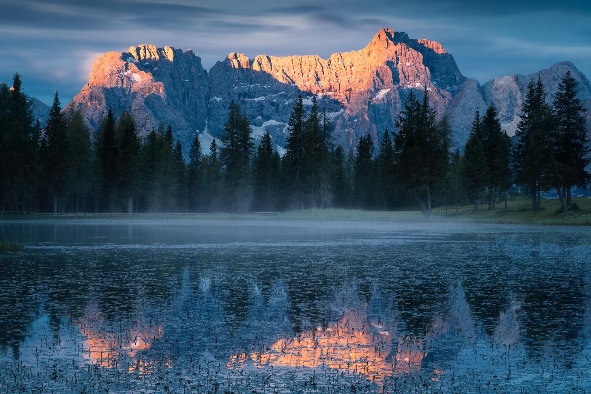 Mountain range reflected in a misty lake at sunrise HD Wallpaper