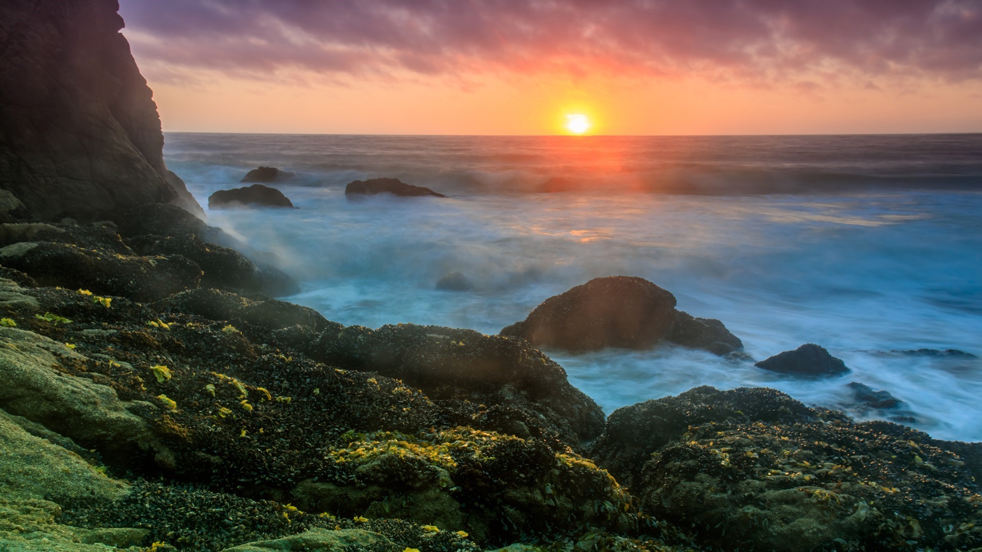 Sunset over the ocean with waves crashing on rocks in California HD Wallpaper