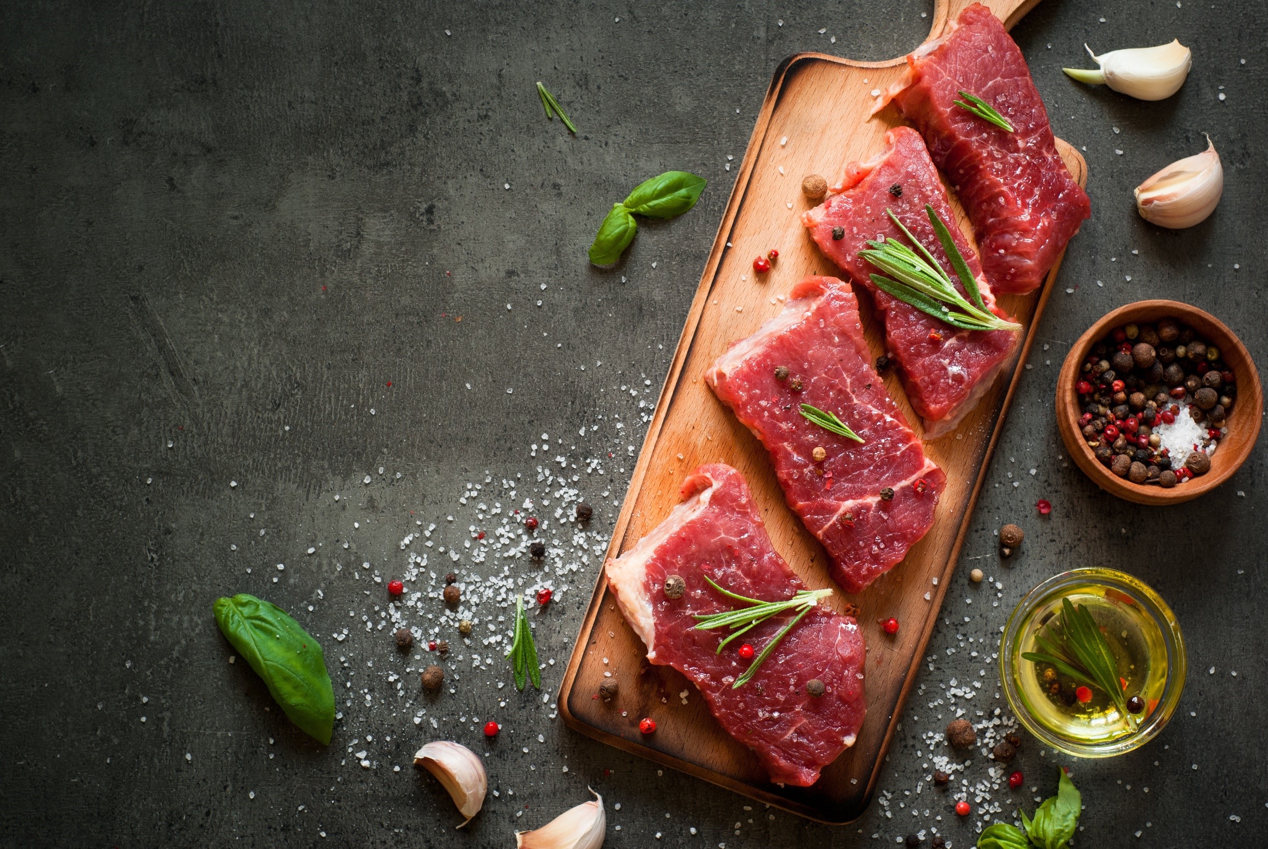 Raw steaks with rosemary, garlic, and spices on a cutting board HD Wallpaper
