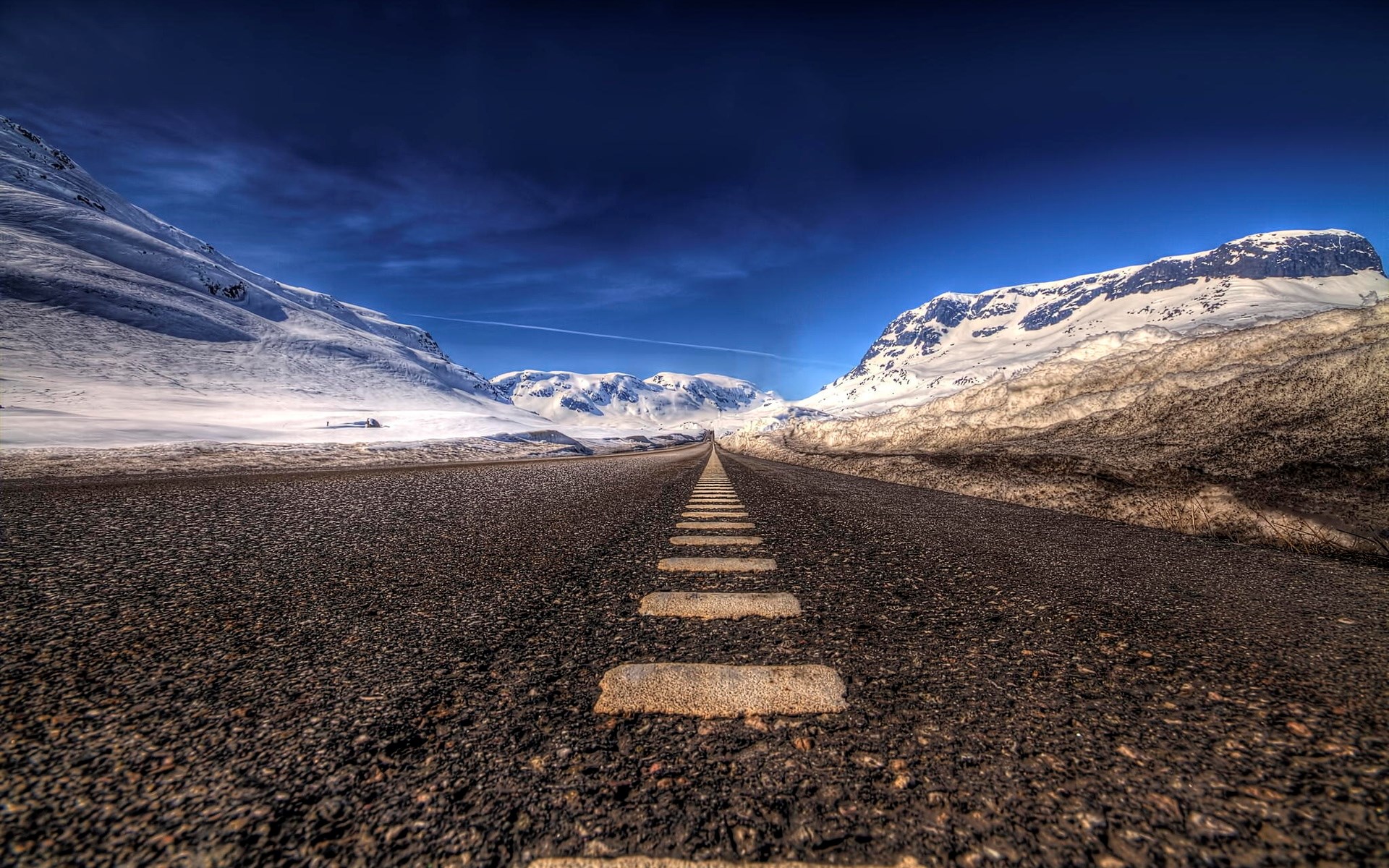 Road through snowy mountains under a dark blue sky HD Wallpaper