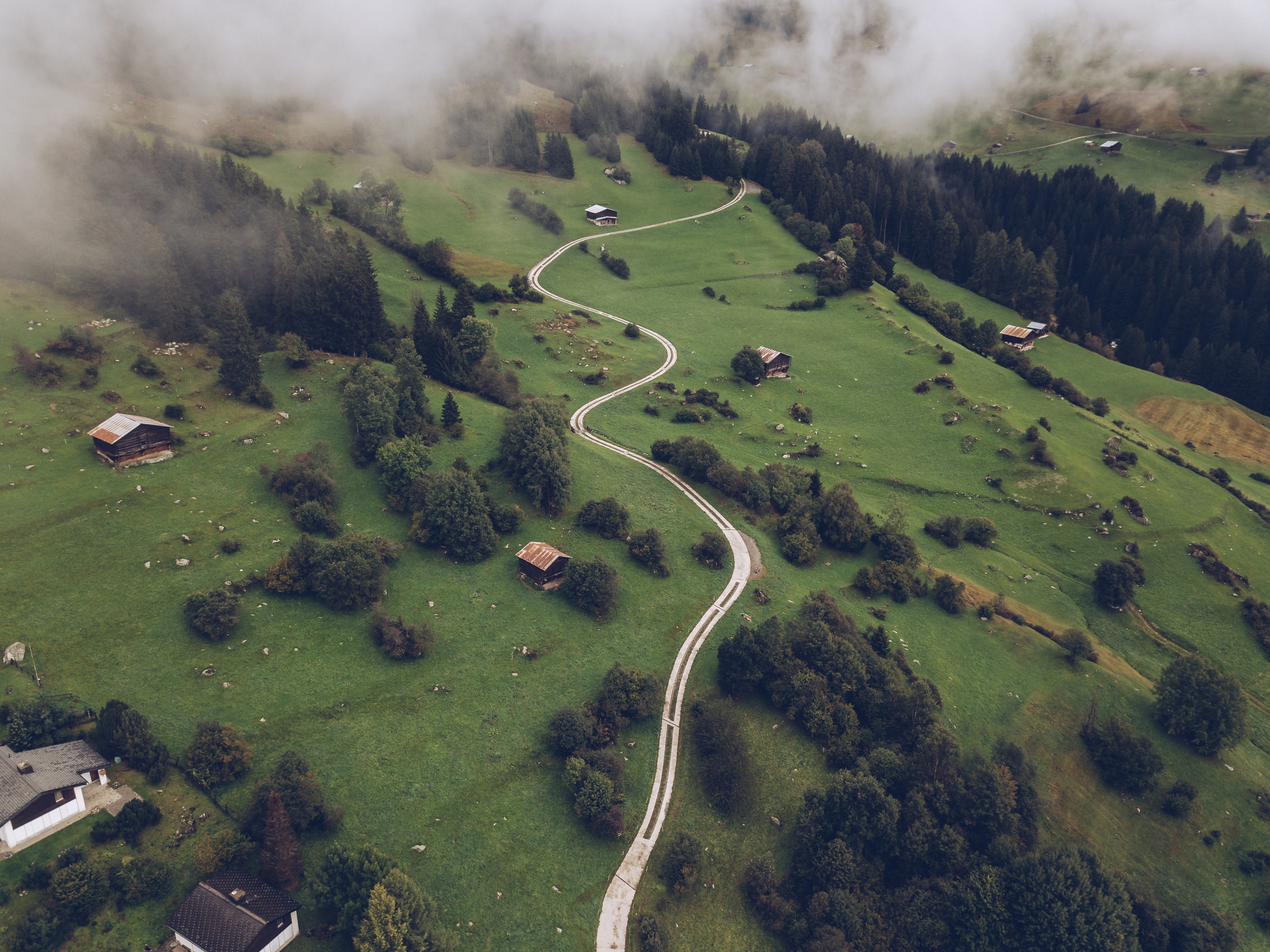 Aerial view of a winding road through a misty Swiss mountain village HD Wallpaper
