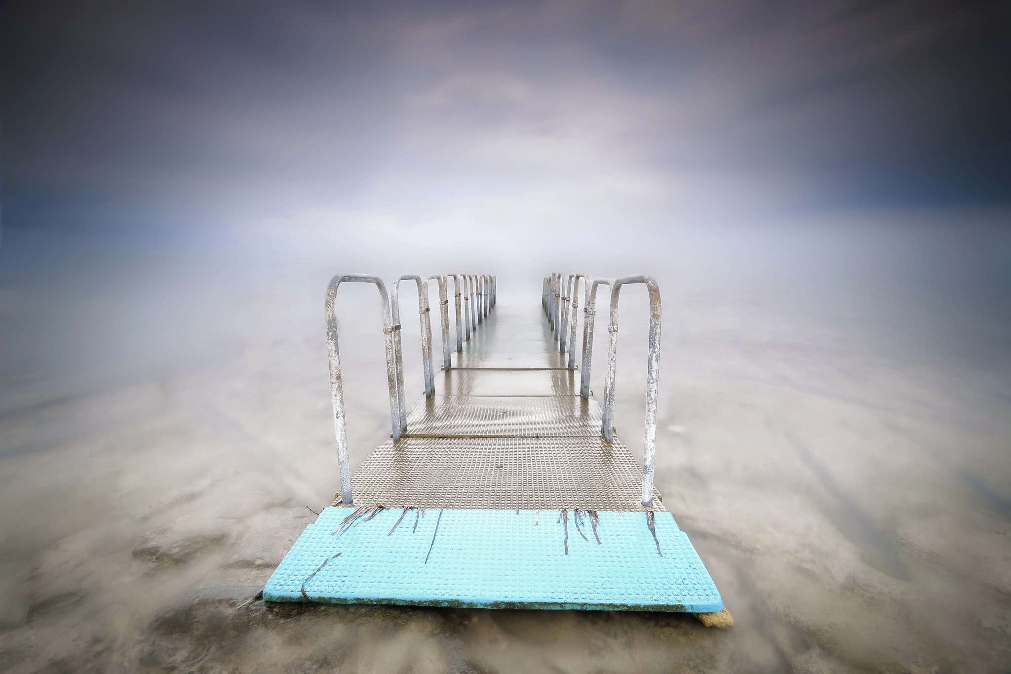 A long pier with railings extends into a misty sea. HD Wallpaper