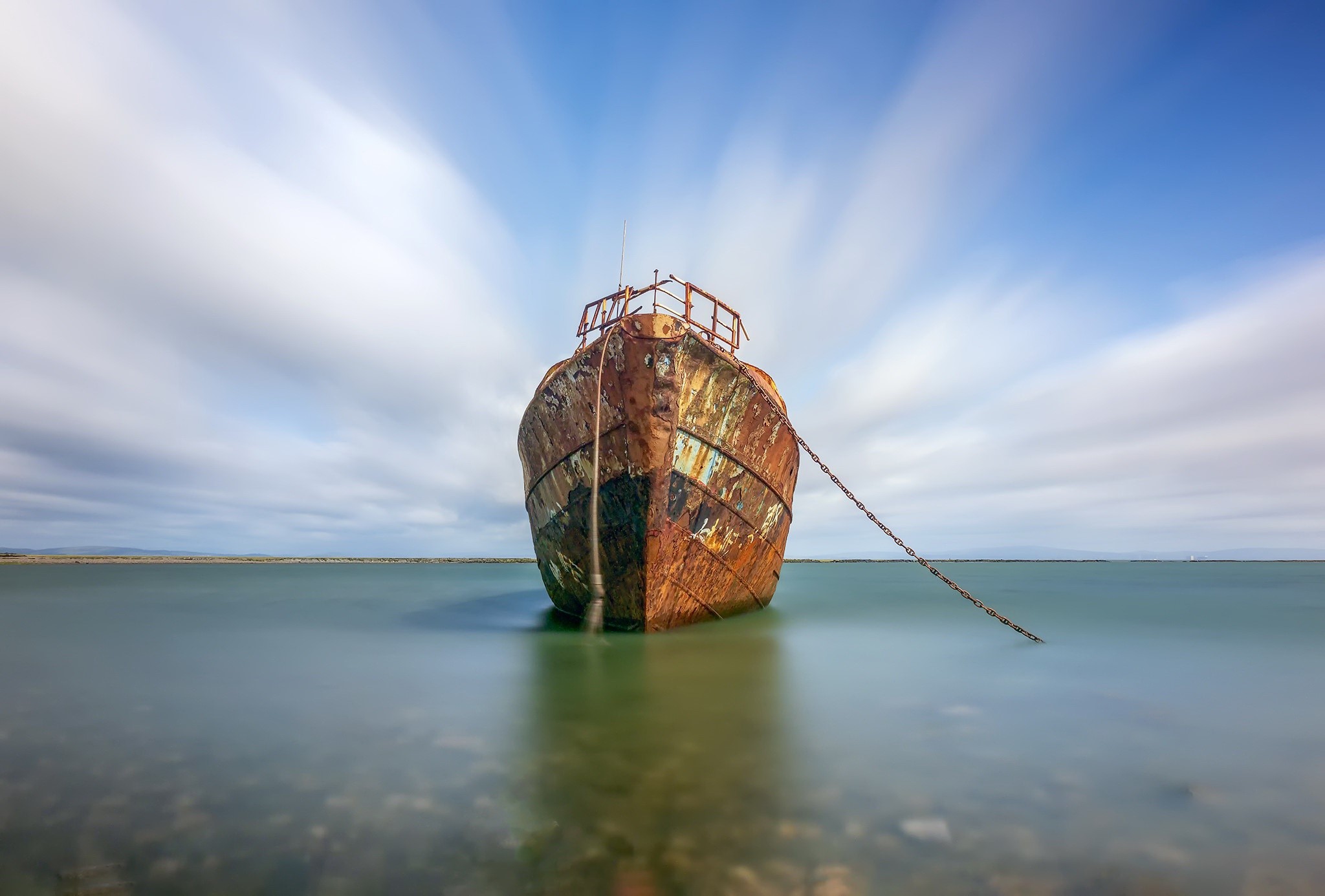 Rusty shipwreck anchored in calm water under a cloudy sky HD Wallpaper