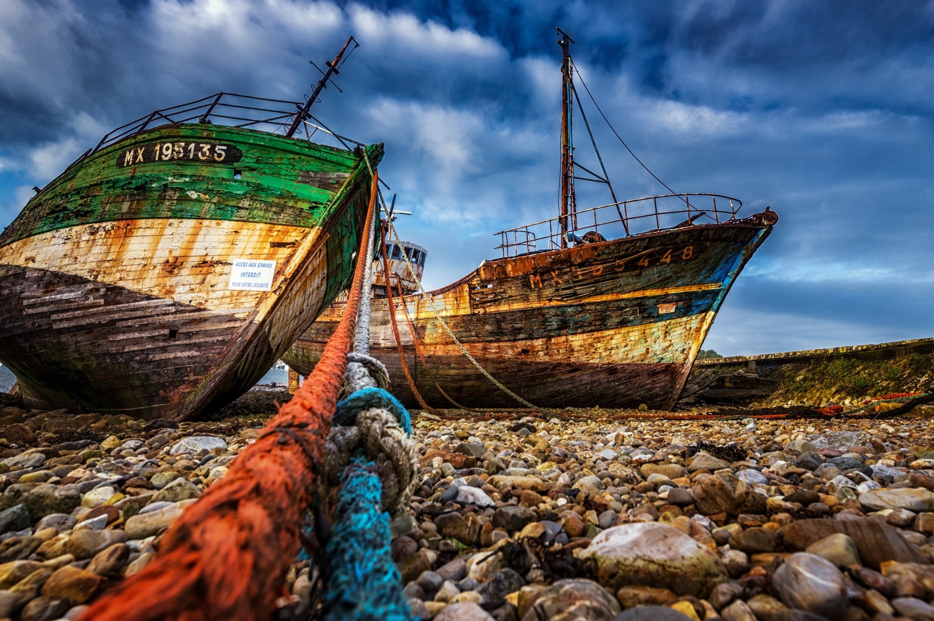 Two abandoned fishing boats on a rocky shore HD Wallpaper