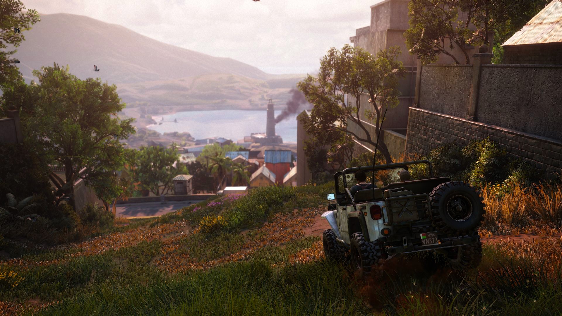 Jeep driving down a hill towards a coastal town with a lighthouse HD Wallpaper
