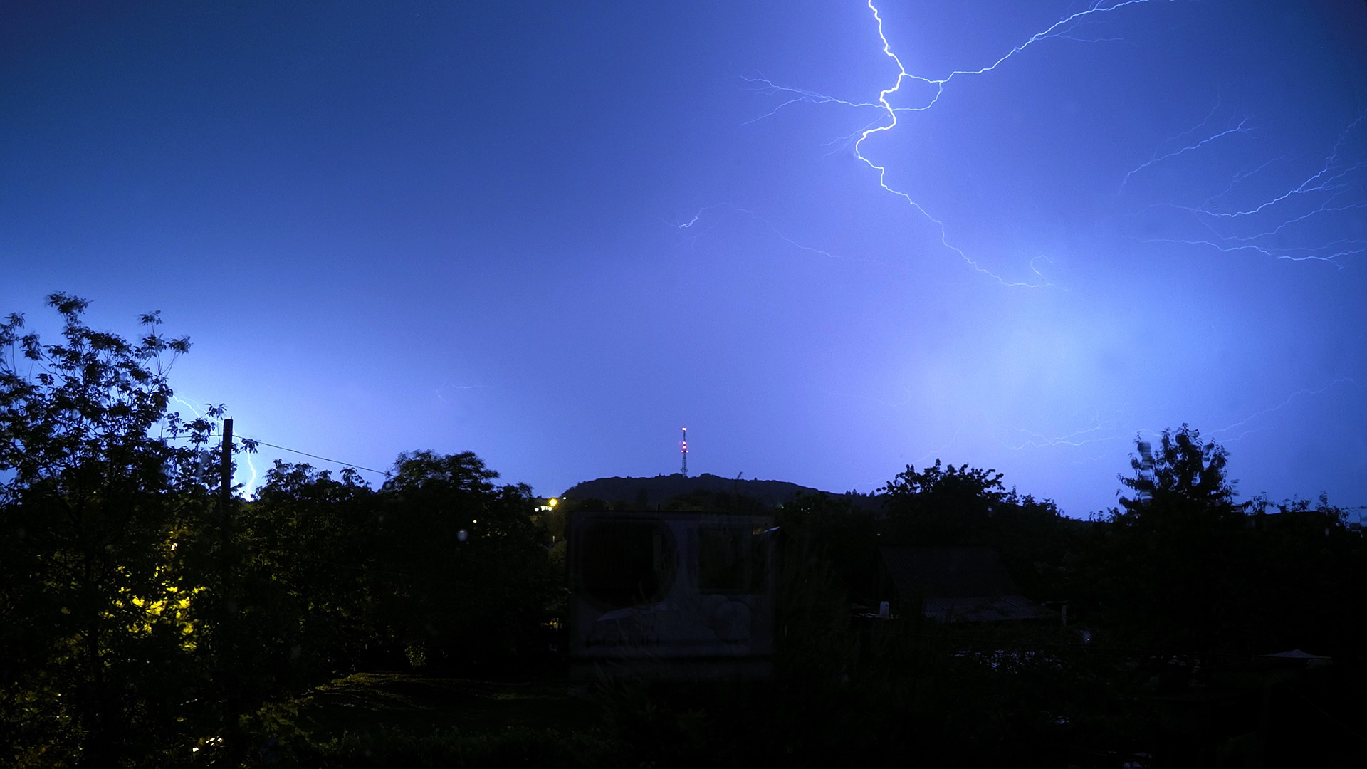 Lightning strikes over a radio tower on a hill at night HD Wallpaper