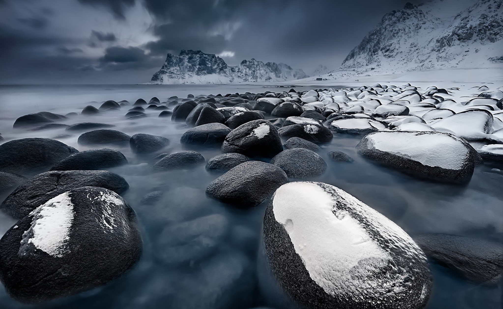 Snow-covered rocks on a cold coast with mountains HD Wallpaper