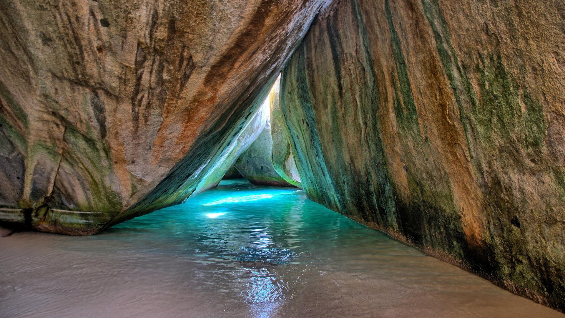 Cave entrance with turquoise water and large boulders HD Wallpaper