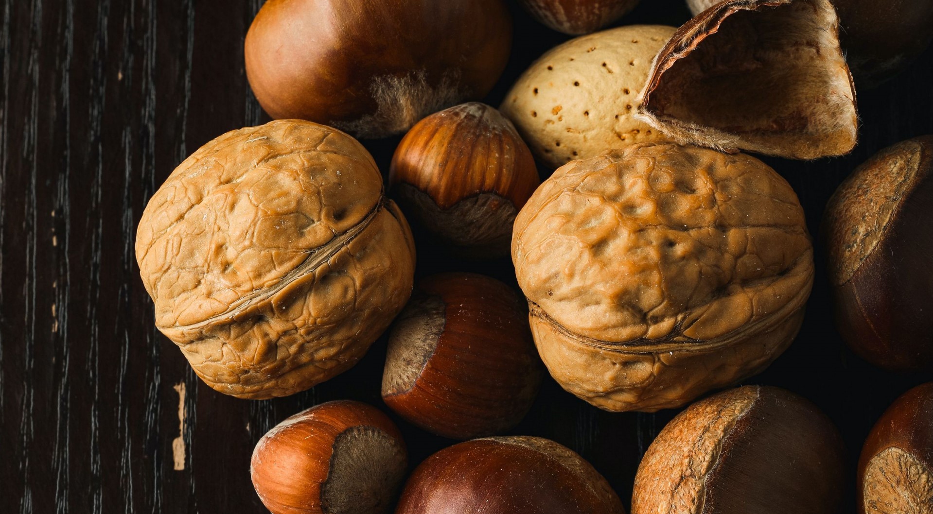 Assortment of nuts on a dark wooden surface HD Wallpaper