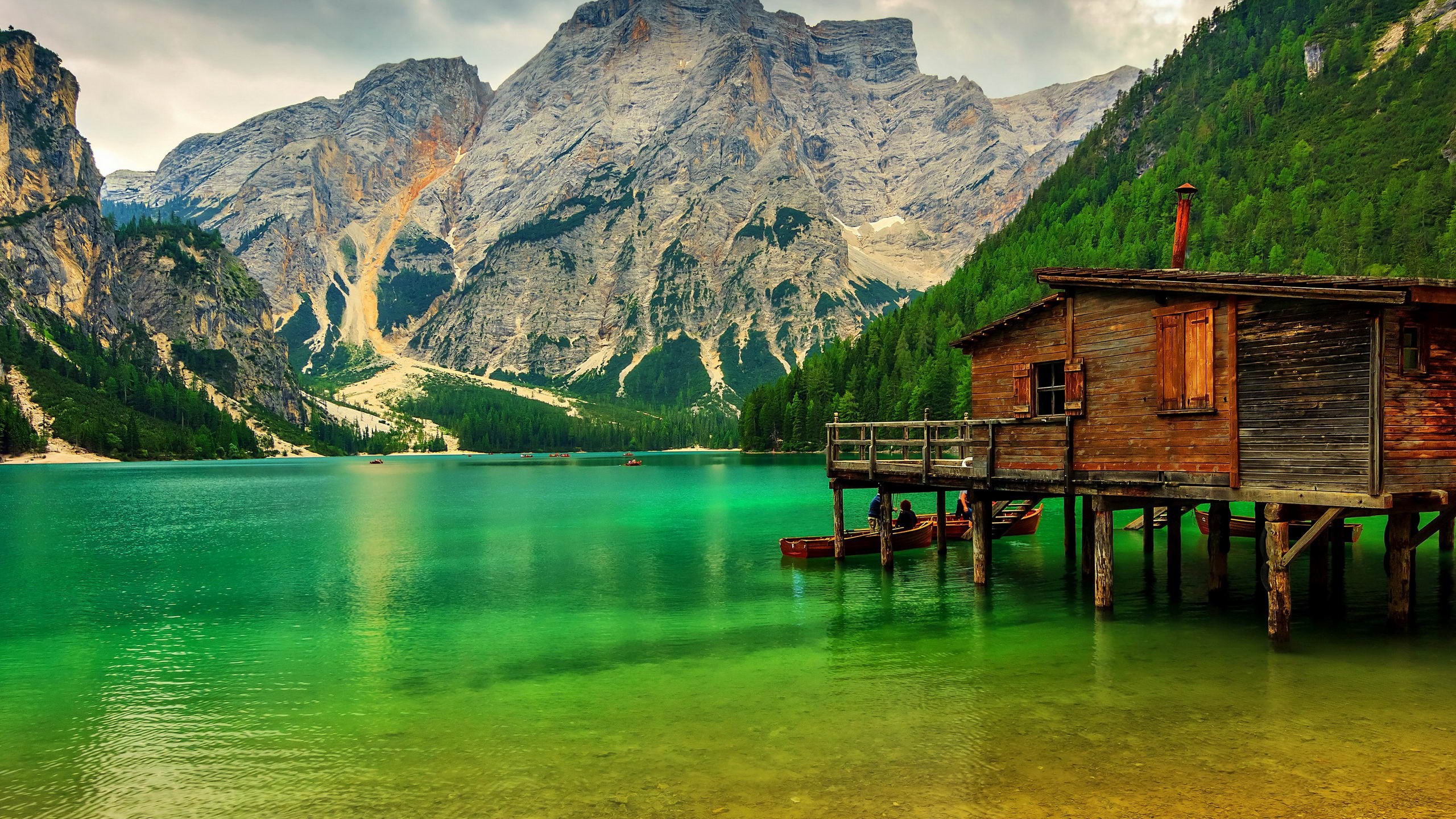 Wooden cabin on stilts by a turquoise lake with mountains HD Wallpaper