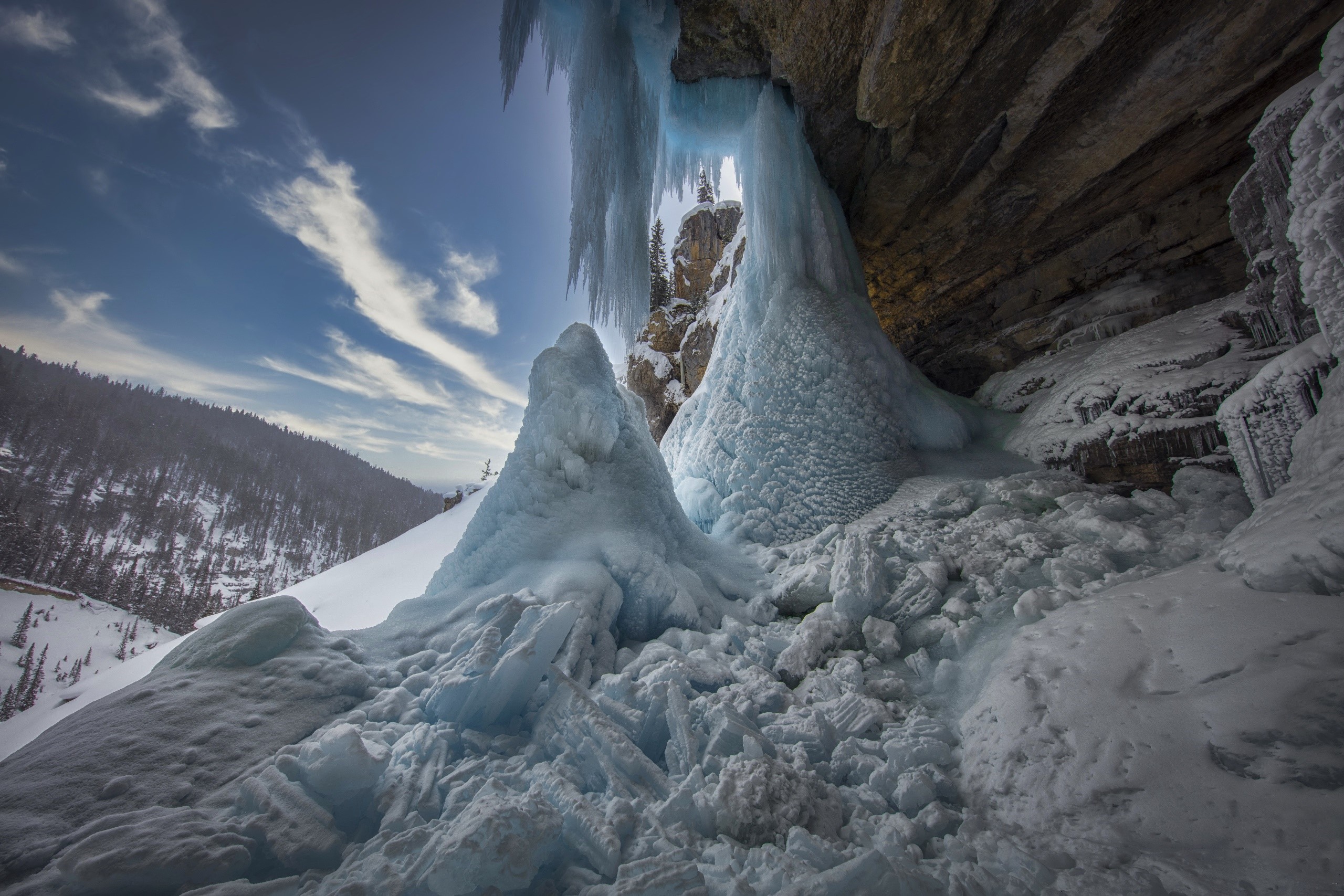 Frozen waterfall cave with icy formations and snowy mountain landscape HD Wallpaper